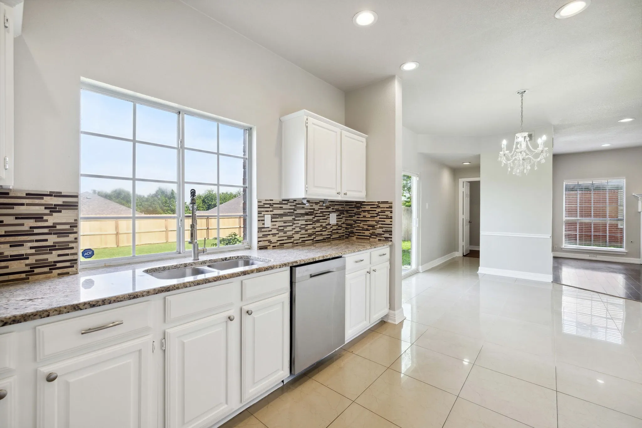 Kitchen featuring decorative light fixtures, white cabinets, backsplash, stainless steel dishwasher, and light stone counters