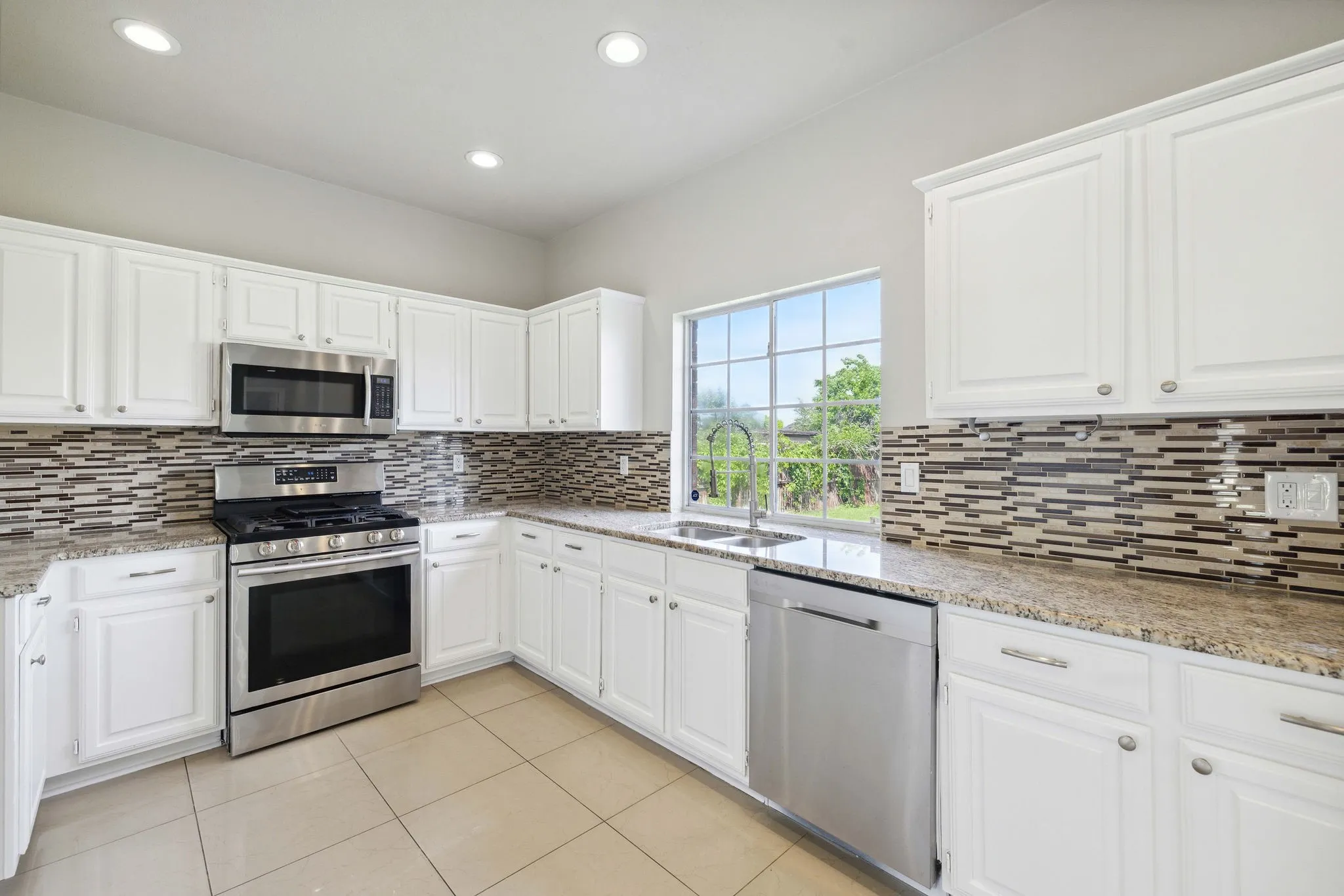 Kitchen featuring appliances with stainless steel finishes, sink, tasteful backsplash, and white cabinets