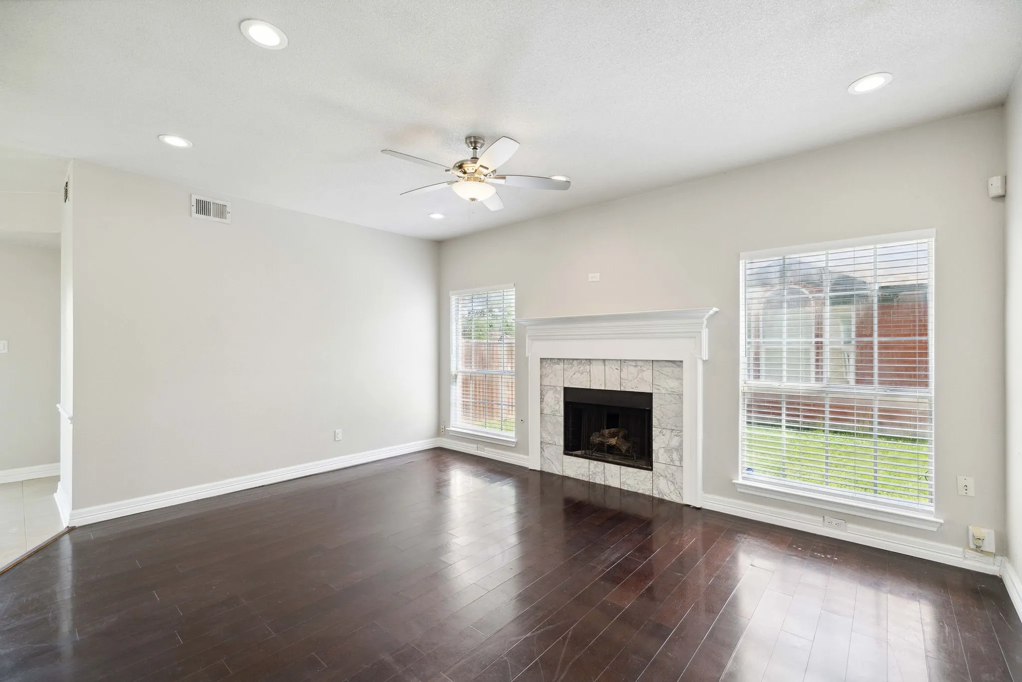Unfurnished living room featuring ceiling fan, a tile fireplace, and dark wood-type flooring