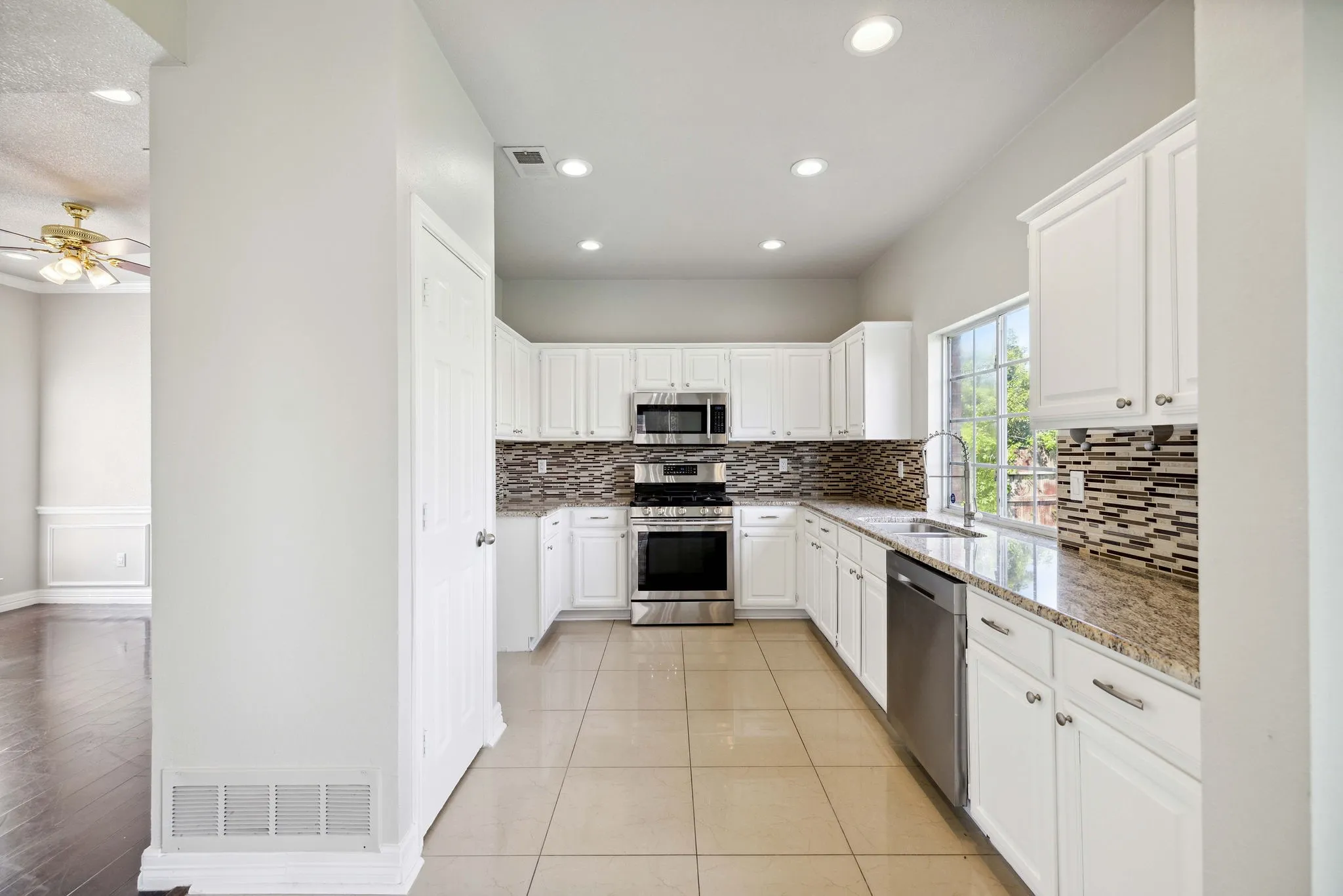 Kitchen with backsplash, stainless steel appliances, light stone counters, white cabinets, and sink