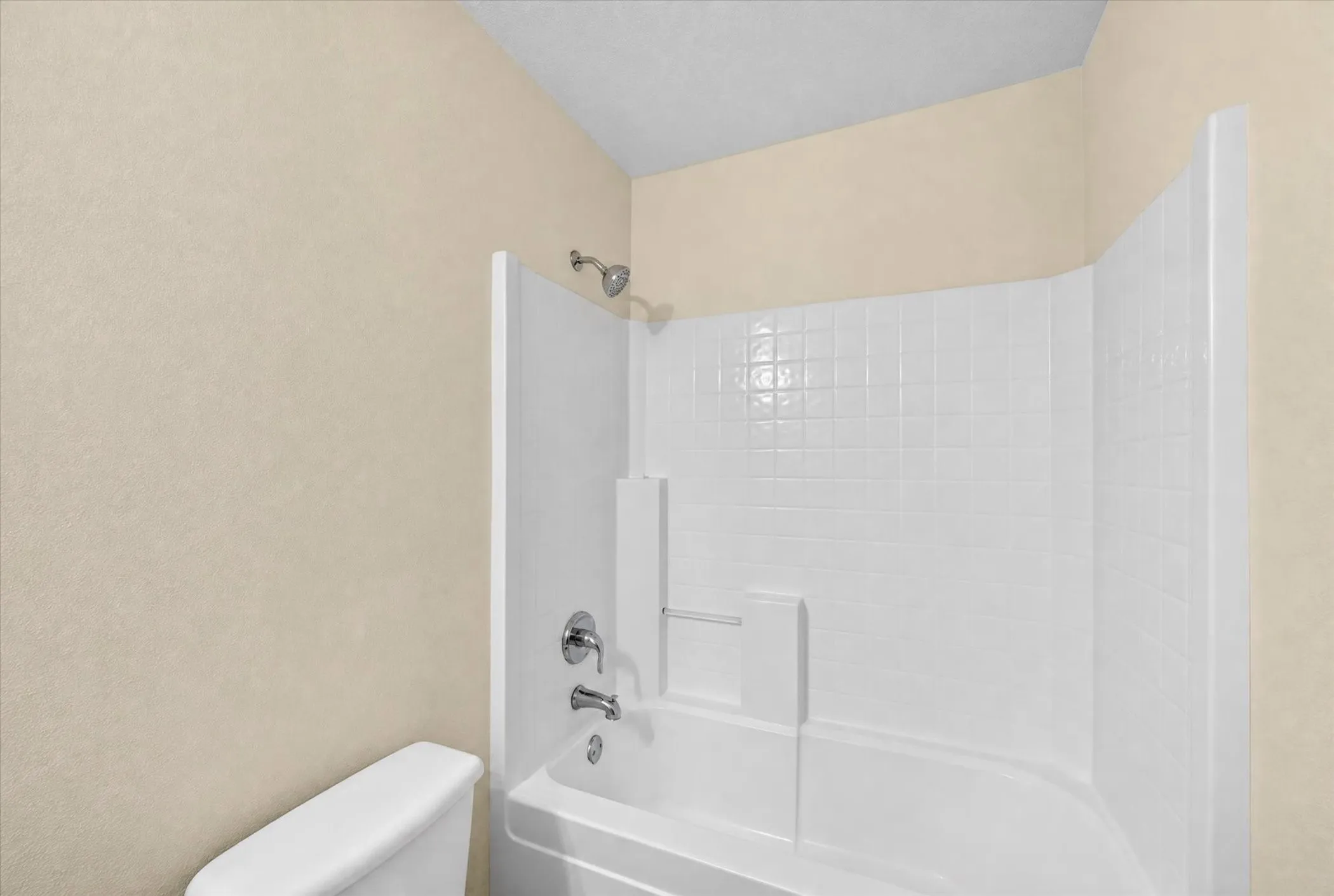 White bathtub with an integrated shower, tiled surround, and chrome fixtures