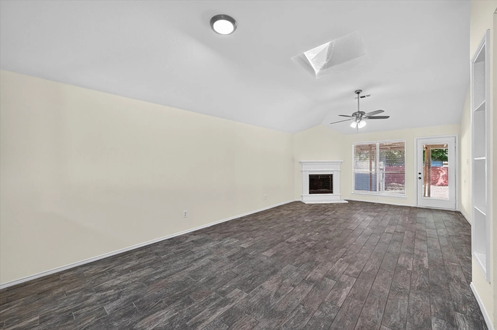 Vaulted ceiling with skylight, wood-finish flooring, fireplace with mantel, ceiling fan, and built-in shelving