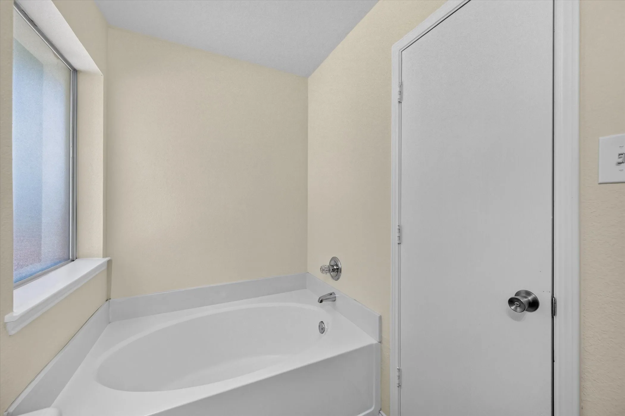 Built-in soaking tub with chrome fixtures, a privacy window, and light-toned wall finishes
