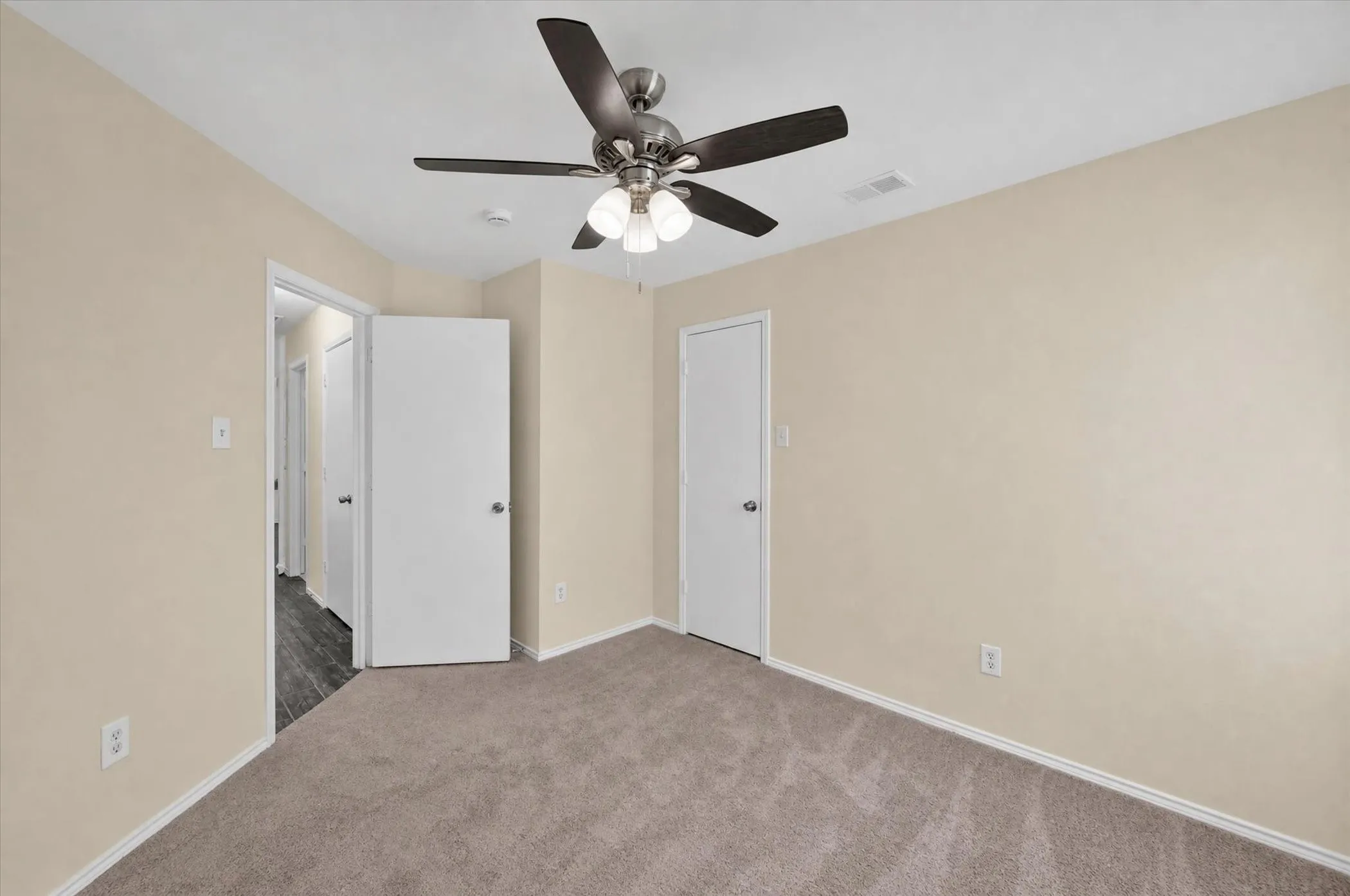 Neutral tone wall paint, carpet flooring, a ceiling fan with integrated lighting, and white interior doors