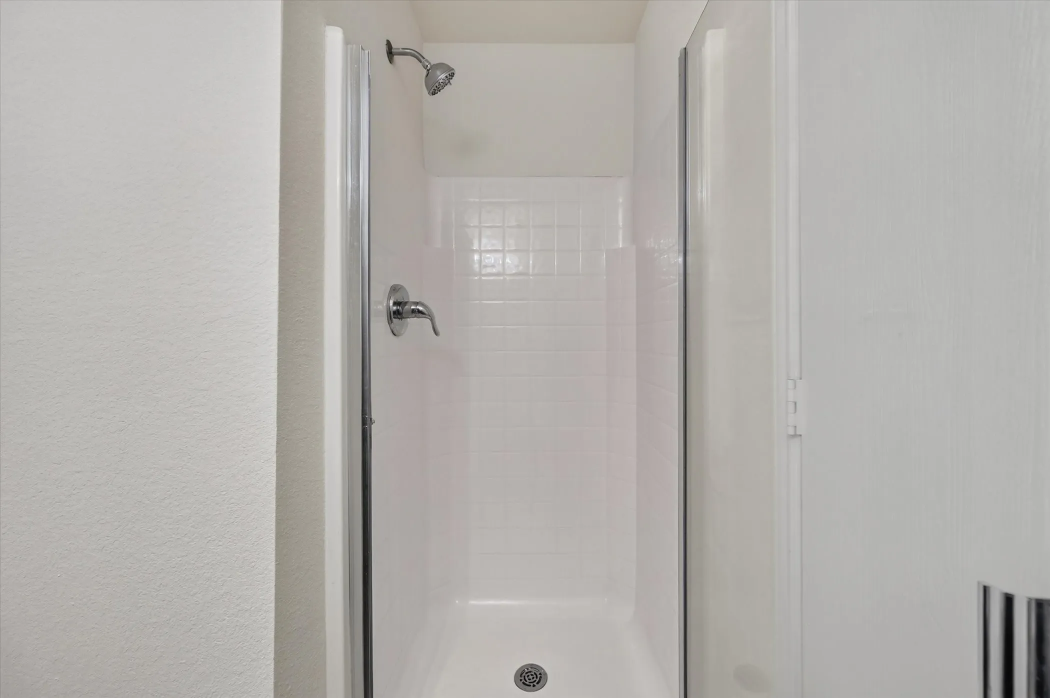 Shower with white subway tile surround, chrome showerhead, and glass enclosure
