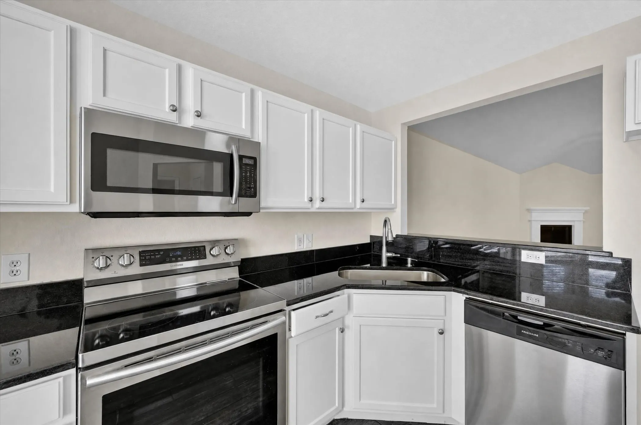 White cabinetry with stainless steel hardware, stainless steel appliances, dark countertops, a dark tile backsplash, and a stainless steel sink with a gooseneck faucet