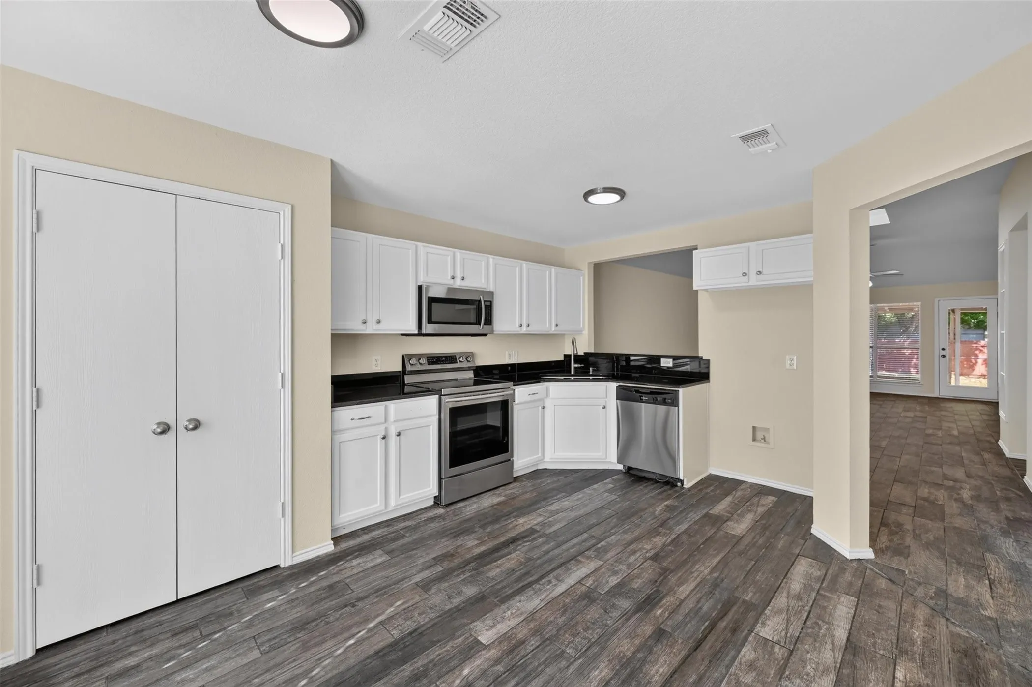 Kitchen featuring stainless steel appliances, dark countertops, white cabinetry, and wood-finish flooring