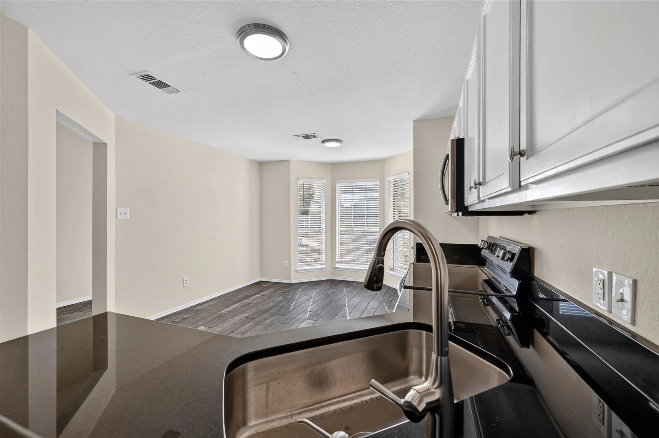 Modern kitchen featuring stainless steel appliances, a deep undermount sink with an arc-pull faucet, dark wood-finish cabinetry, and dark countertops