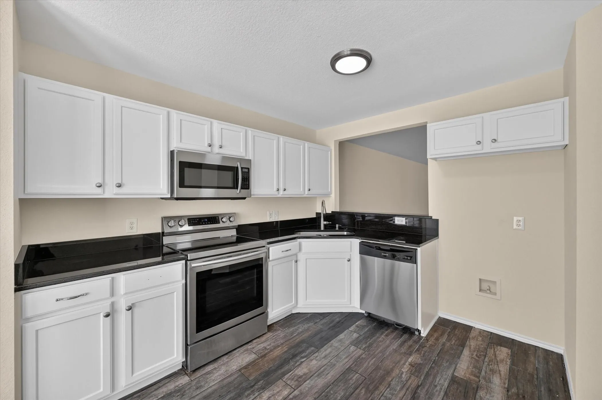White cabinetry, dark stone countertops, stainless steel appliances, stainless steel sink, and wood-finish flooring