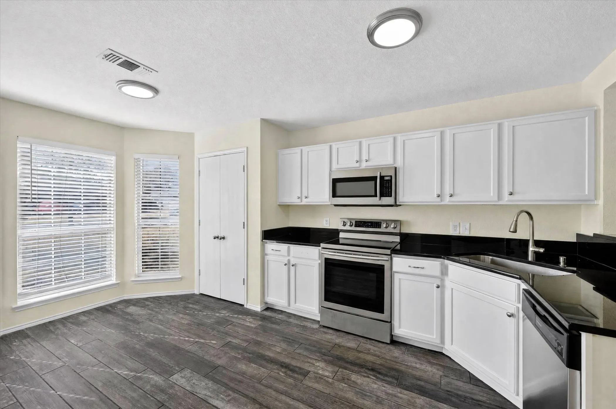Kitchen featuring dark wood-finish flooring, white cabinetry, dark countertops, and stainless steel appliances
