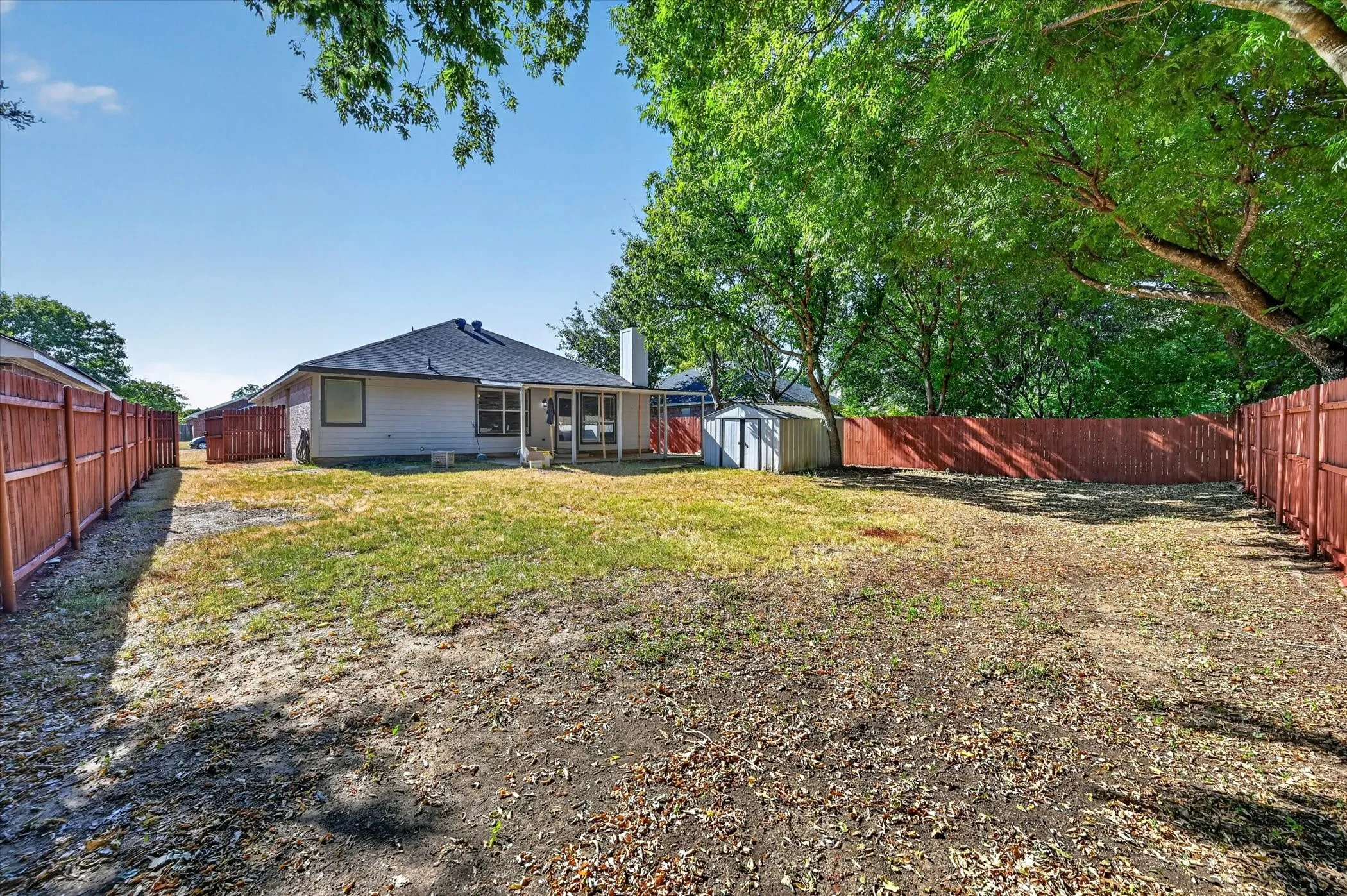 Expansive backyard with a covered patio, storage shed, and perimeter fencing