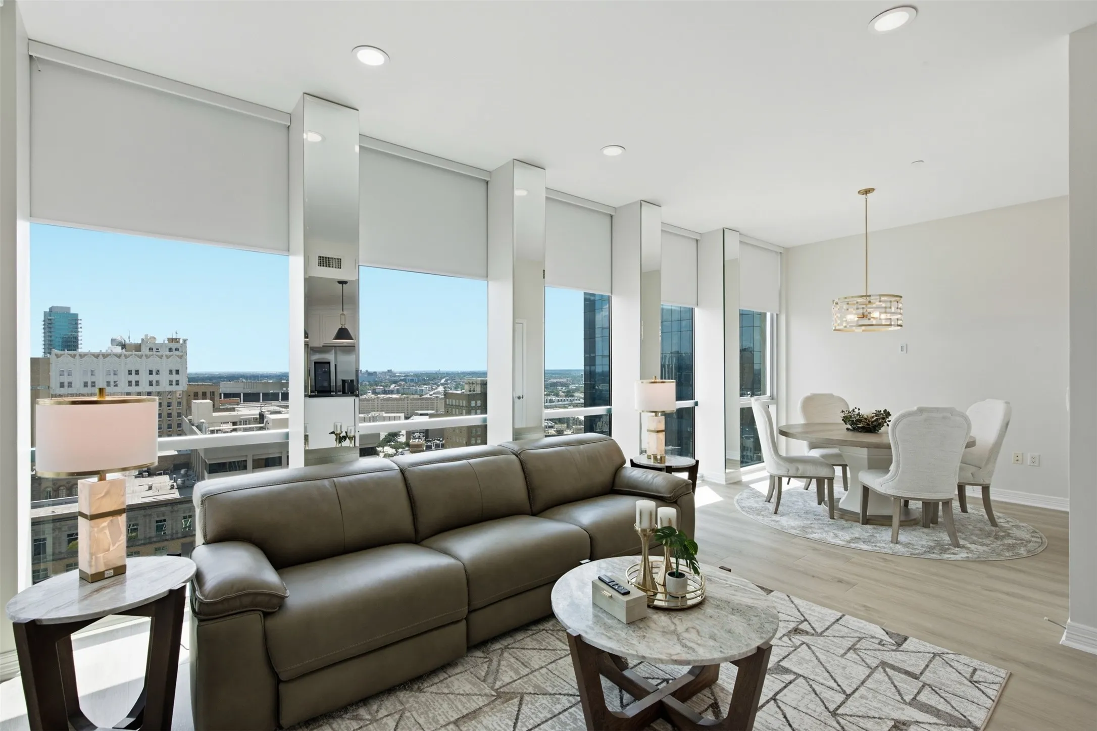 Expansive floor-to-ceiling windows with roller shades, light wood-finish flooring, recessed lighting, and a dining area with a contemporary chandelier