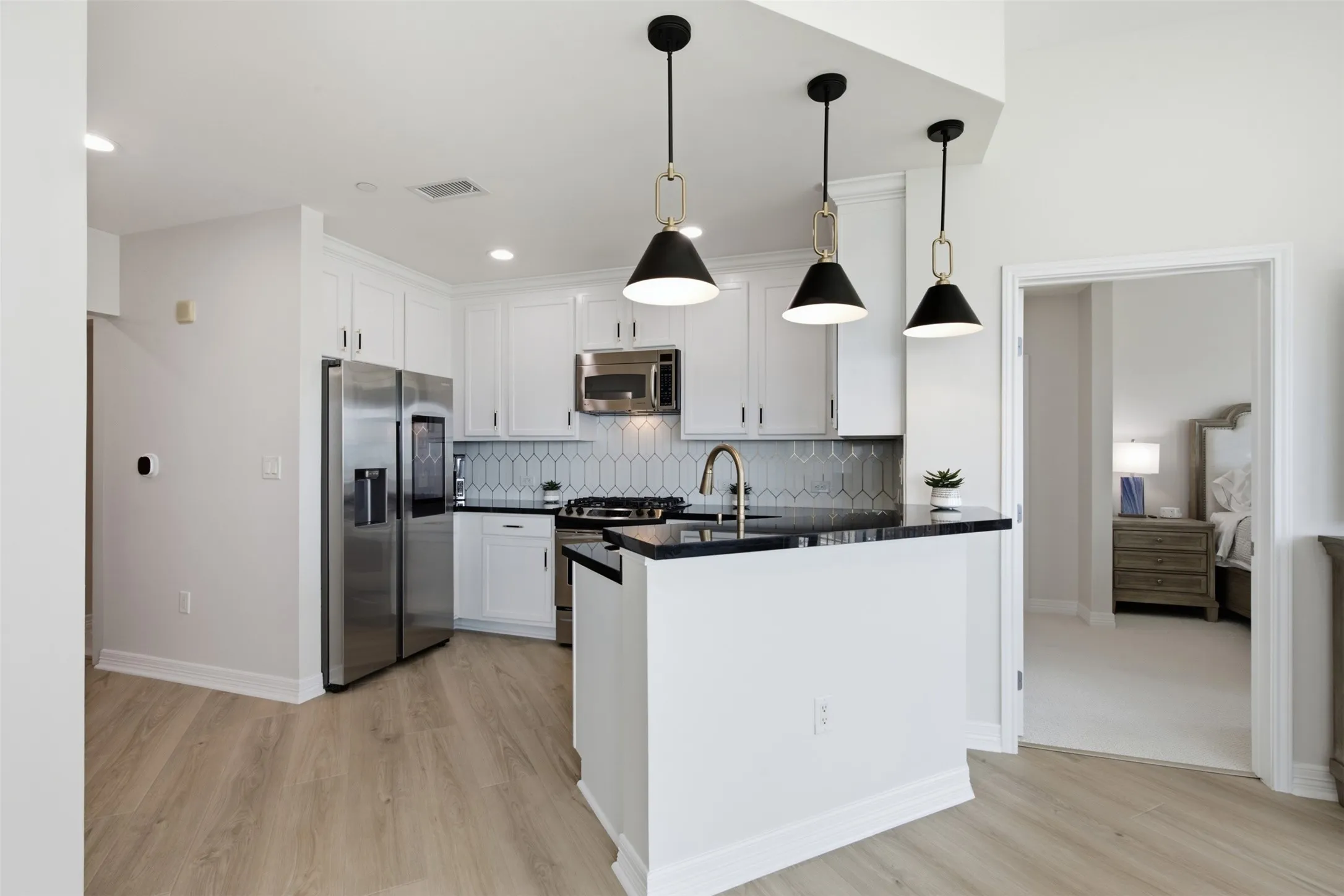 Modern kitchen featuring white cabinetry, black quartz countertops, stainless steel appliances, and a waterfall-edge island