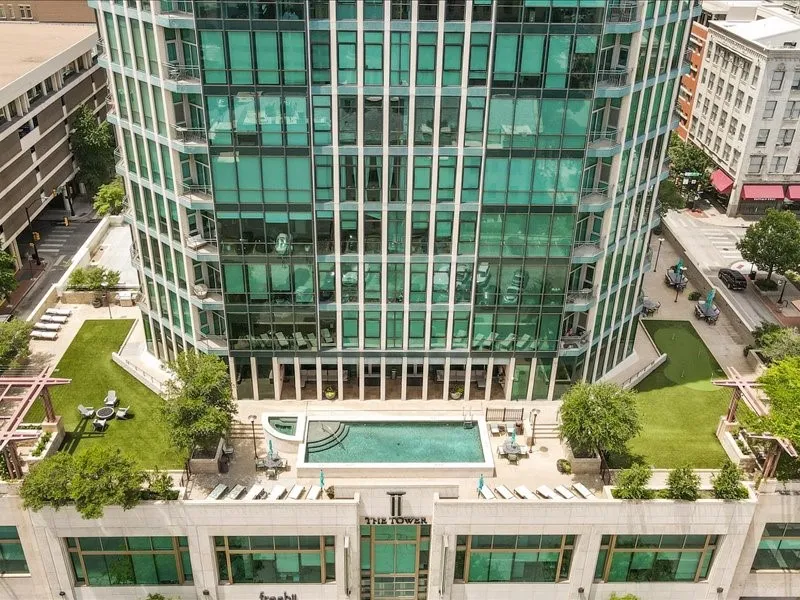 Modern high-rise with a sleek glass exterior, featuring multiple rooftop terrace areas with artificial turf, a swimming pool, and dedicated lounge spaces