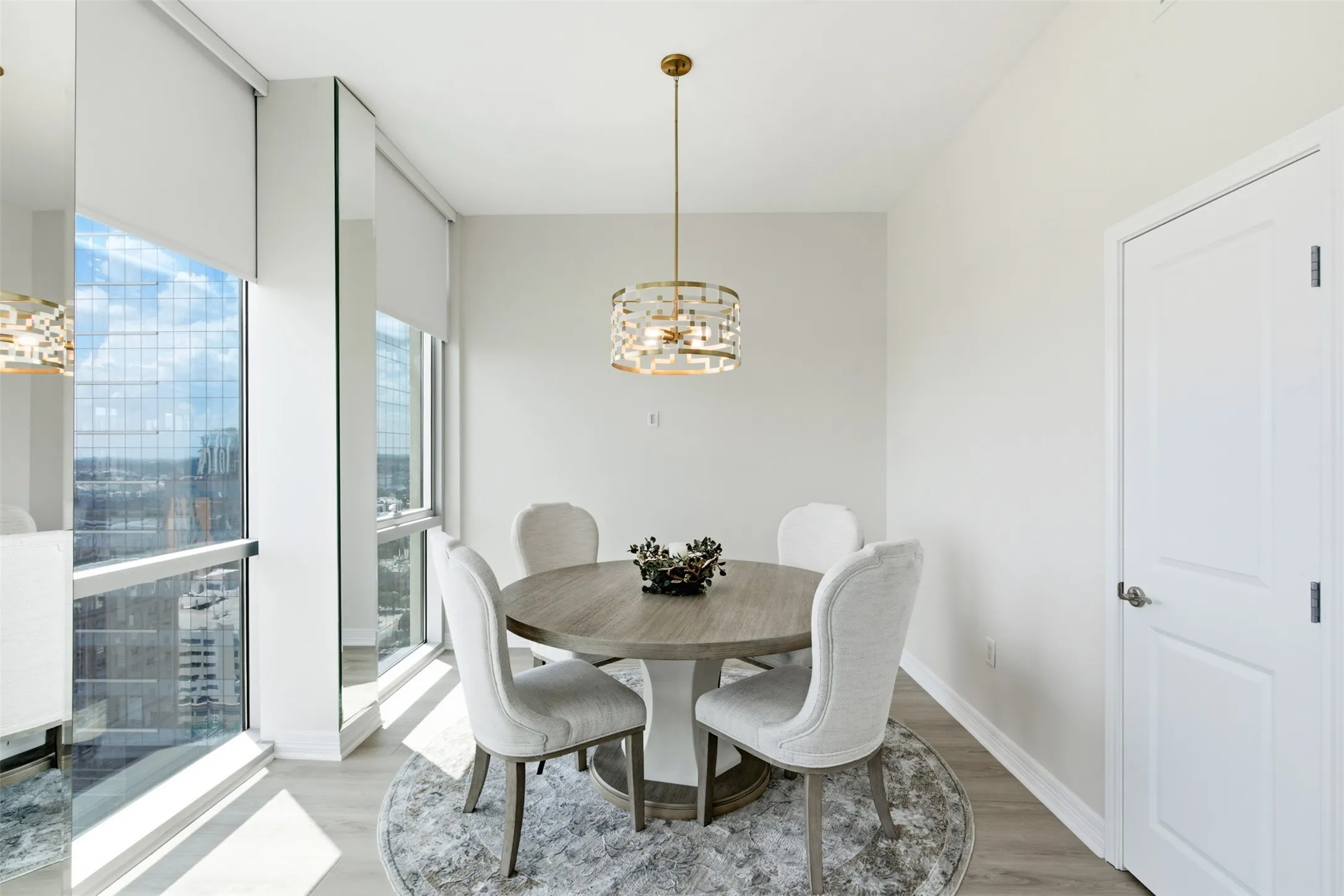 Floor-to-ceiling windows with roller shades, light wood-finish flooring, and a decorative pendant light fixture