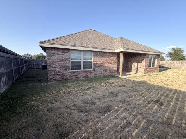 Brick exterior with a covered patio, fenced backyard, and a shingle roof