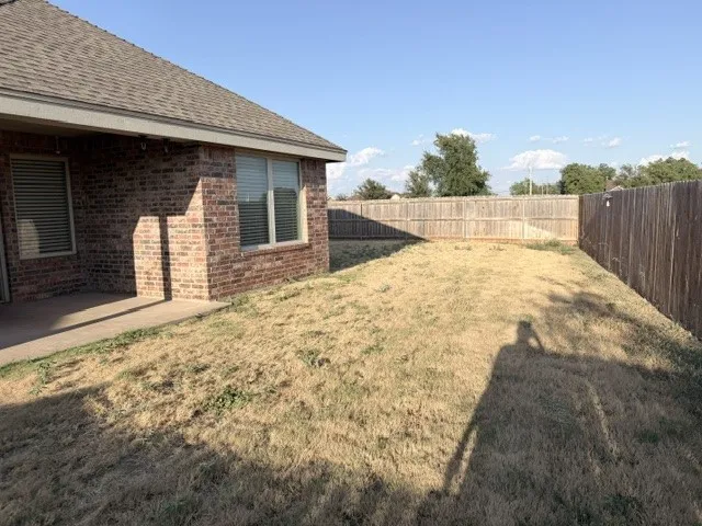 Brick exterior with a covered patio, fenced backyard, and shingle roof