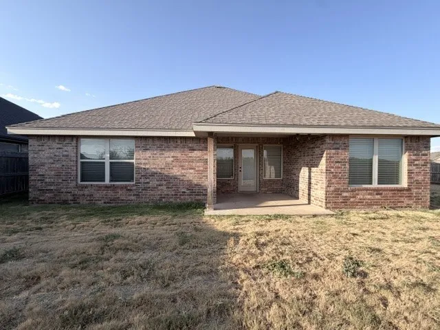 Brick exterior with composition shingle roof, windows with blinds, and a covered patio