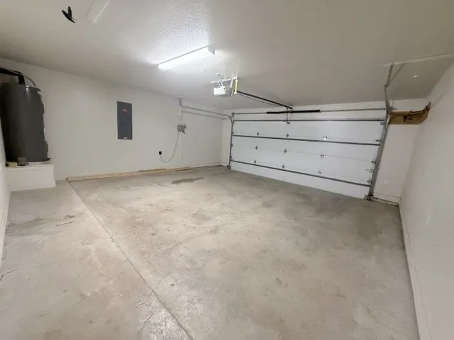 Attached garage with concrete flooring, overhead fluorescent lighting, and a white paneled garage door