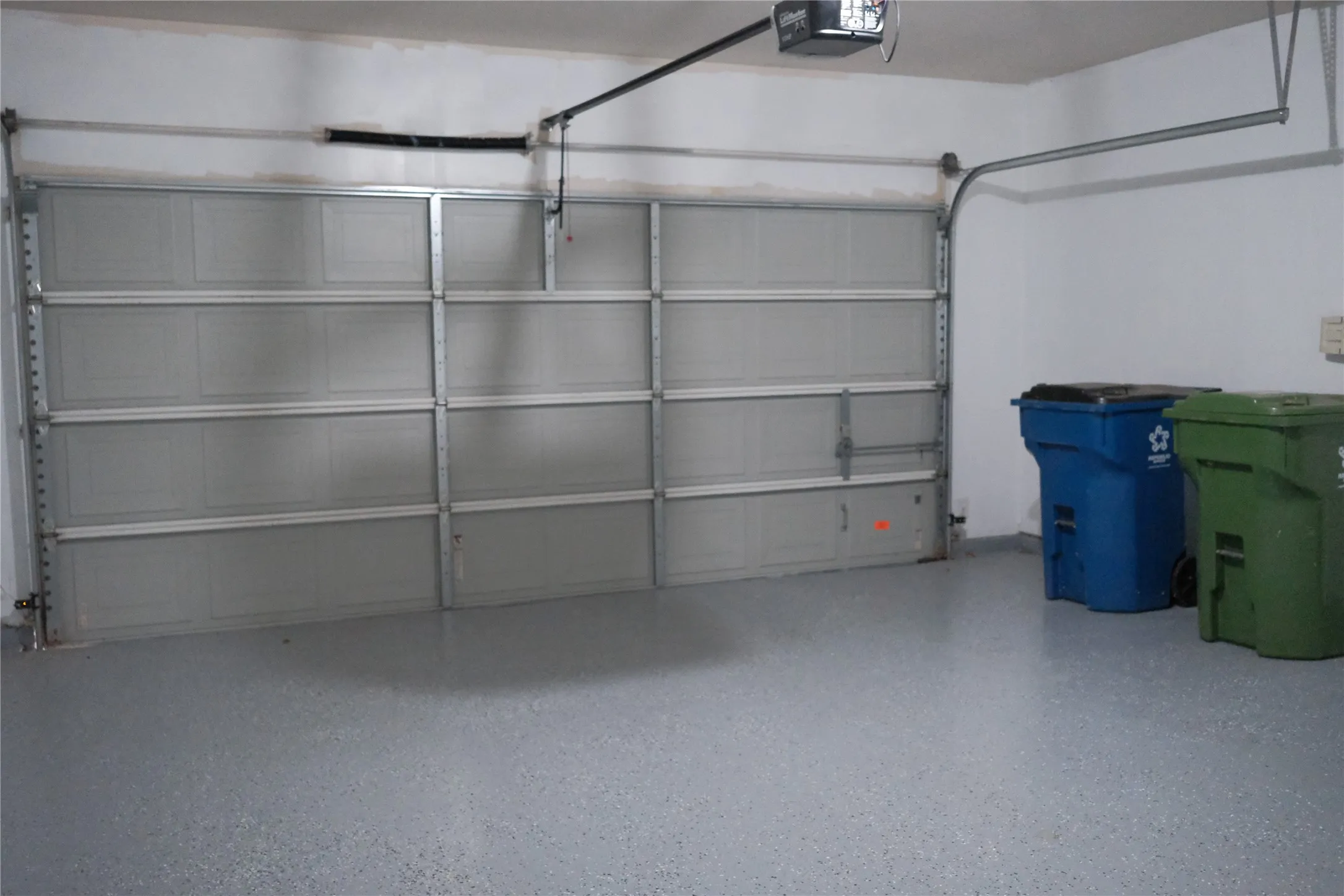 Garage featuring an automatic opener, a sectional garage door, and a speckled floor finish