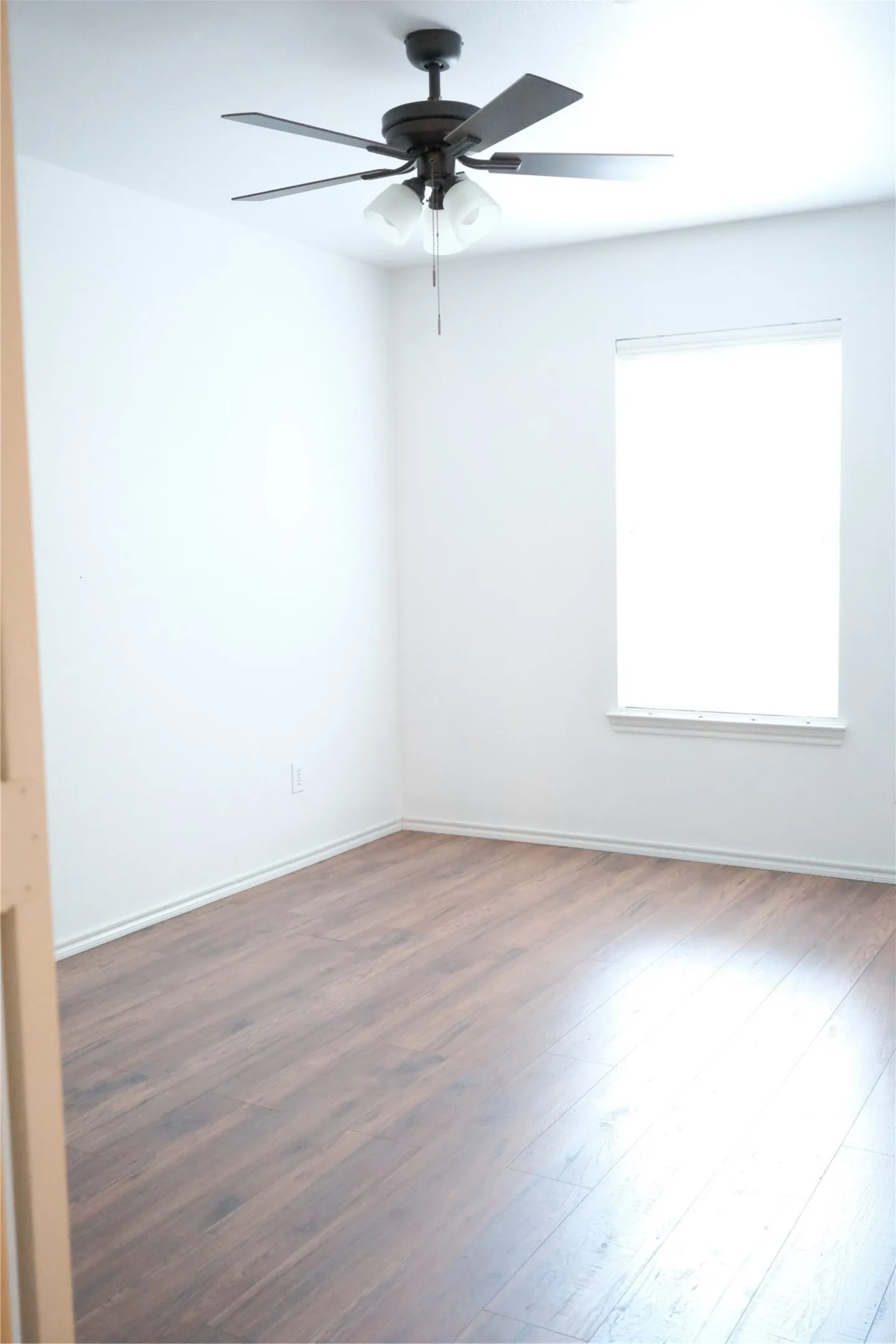Wood-finish flooring throughout, a ceiling fan with integrated lighting, and a single window with white trim