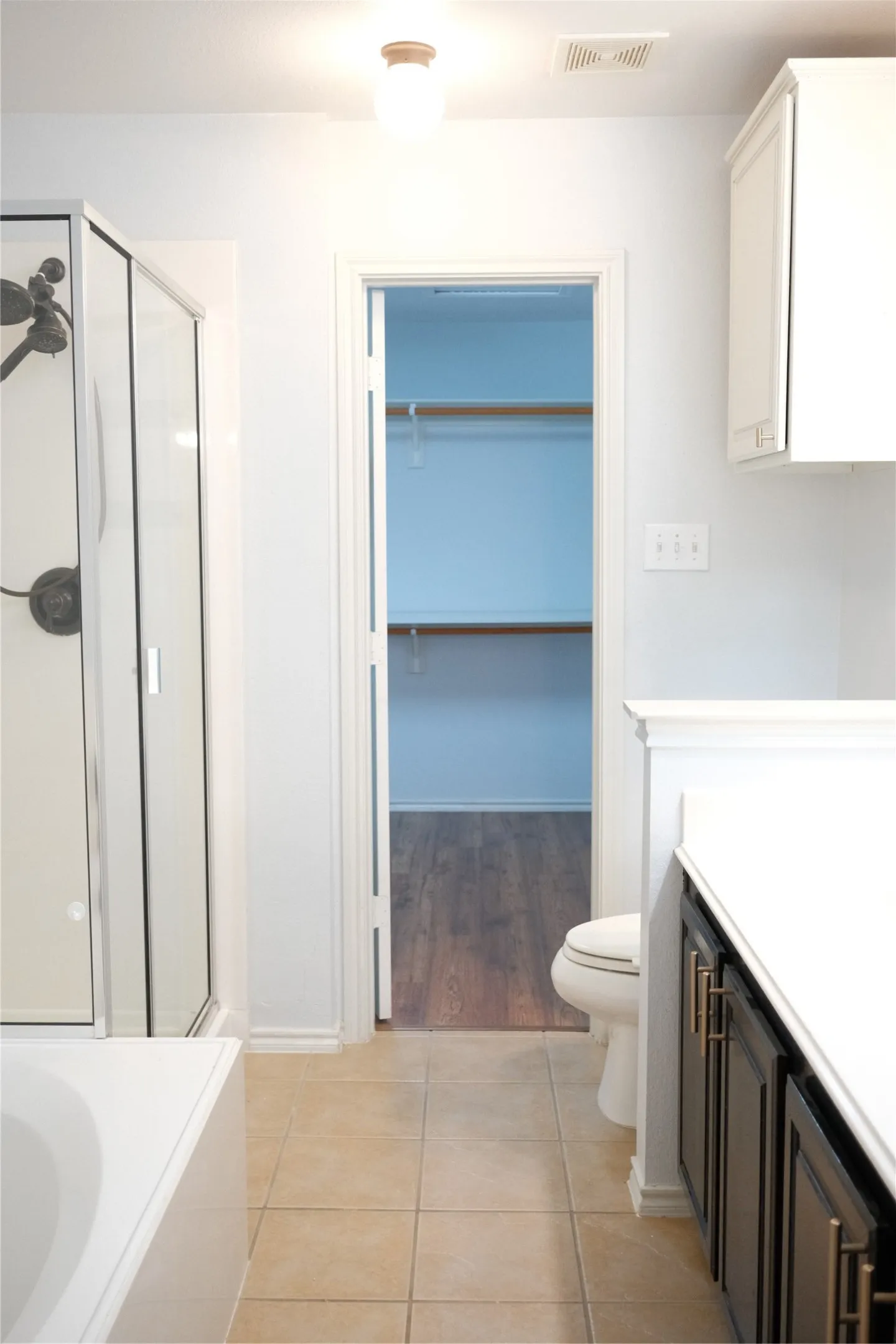 Bathroom featuring a shower enclosure, white bathtub, dark wood-finish vanity with a white countertop, and tile flooring