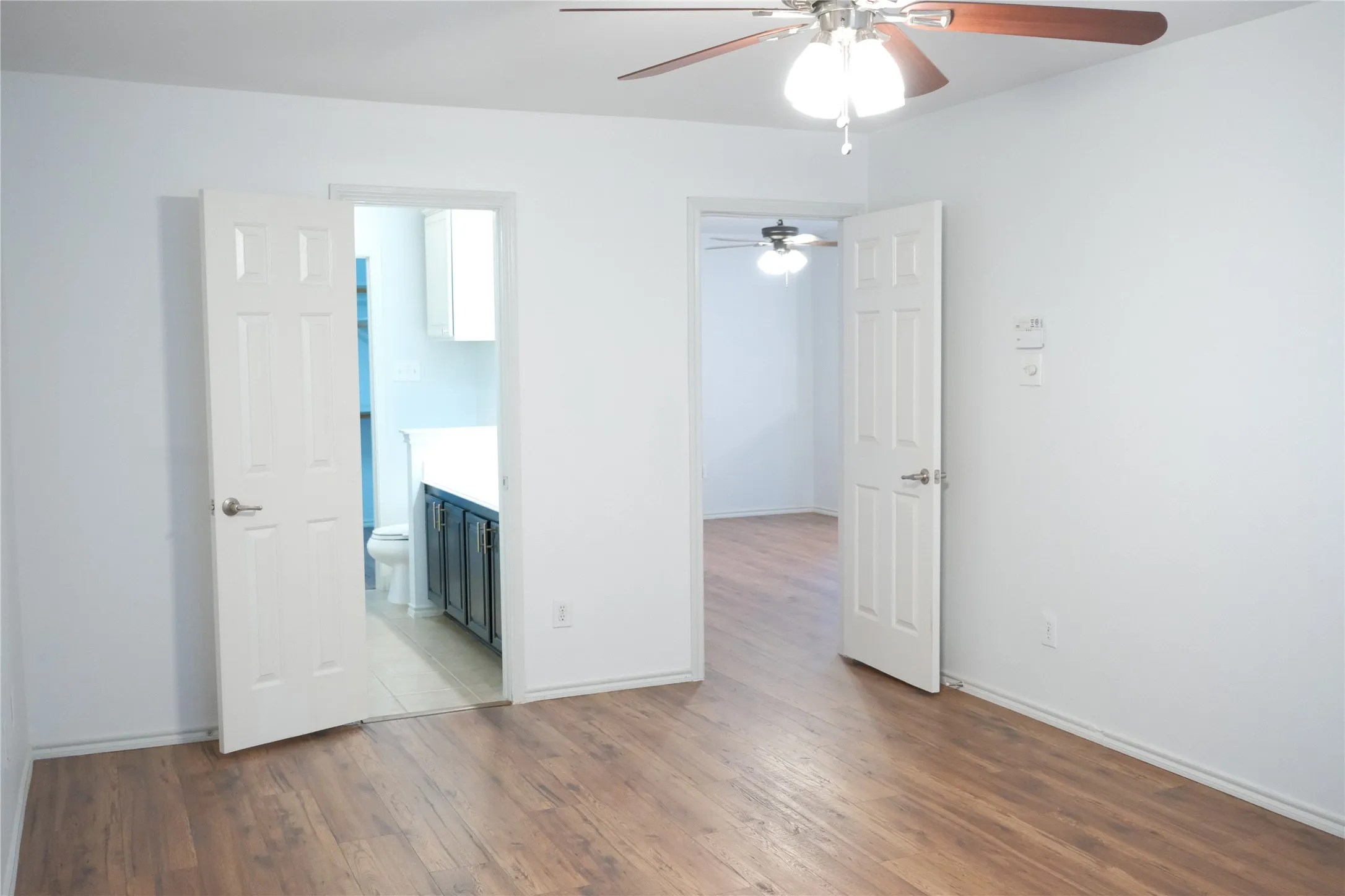 Wood-finish flooring throughout, bright white walls, and a ceiling fan with integrated lighting