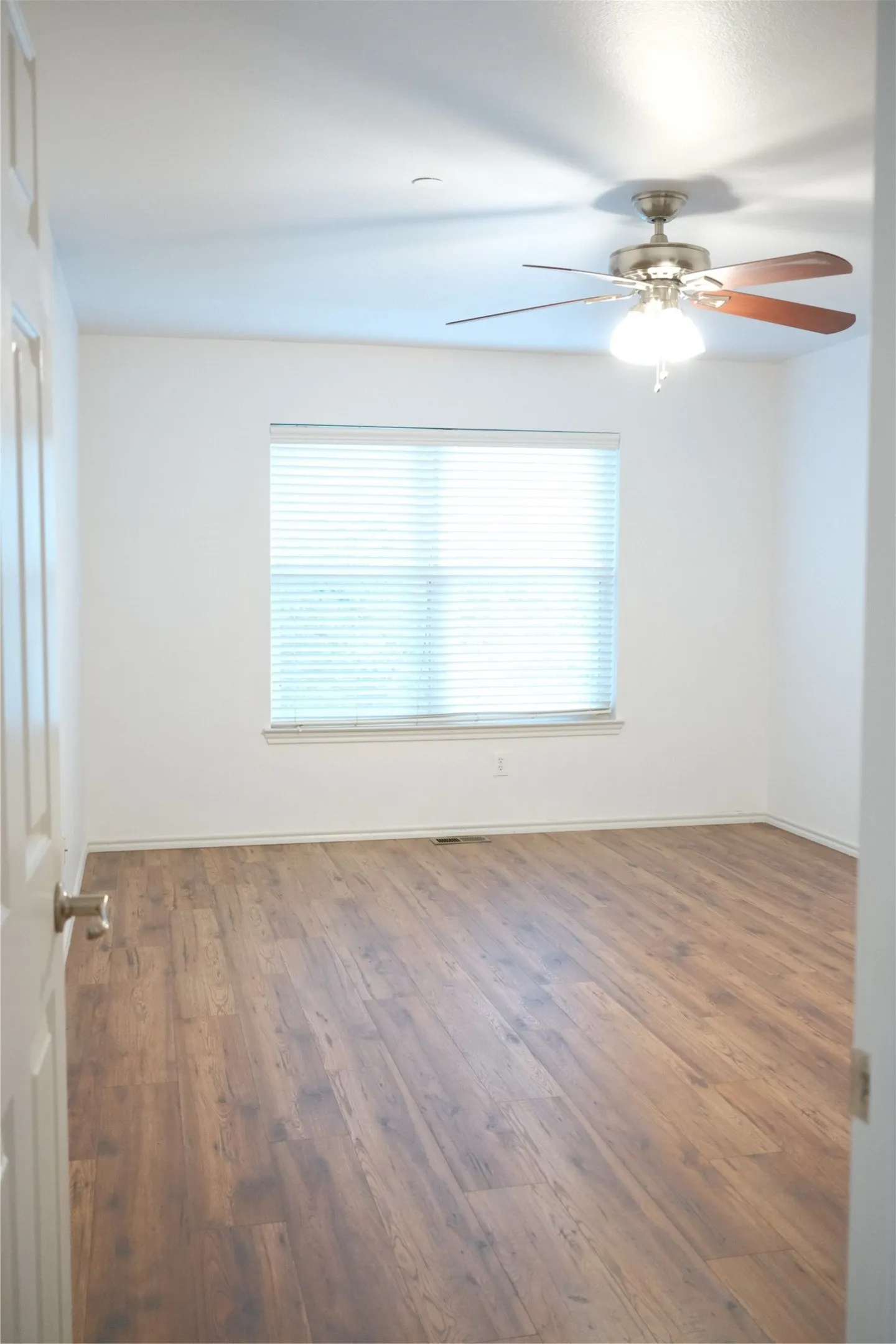 Spacious room featuring wood-finish flooring, a window with blinds, and a ceiling fan with integrated lighting