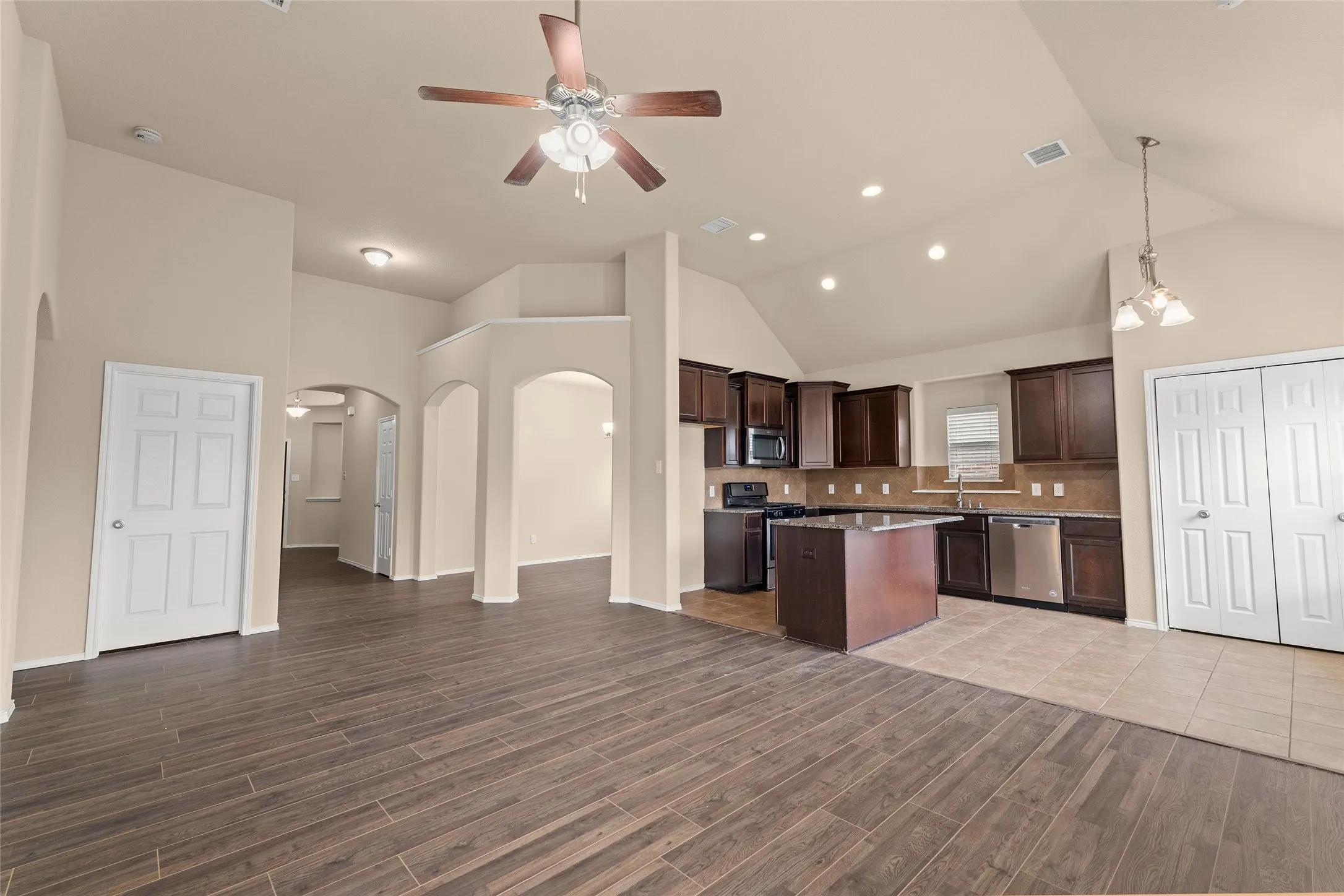 Kitchen with arched walkways, open floor plan, pendant lighting, dark brown cabinets, and a center island