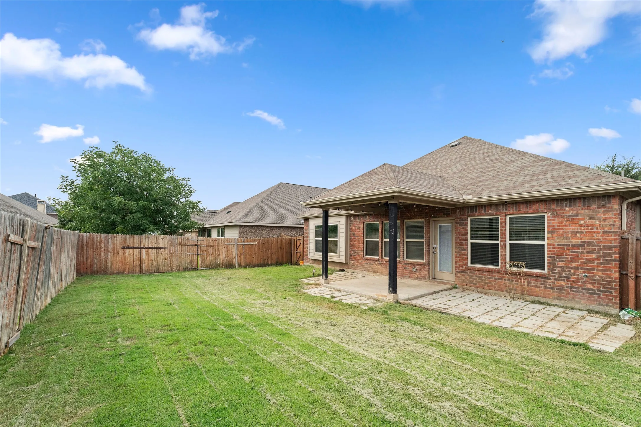 Back of property featuring brick siding, a fenced backyard, a patio, and a shingled roof