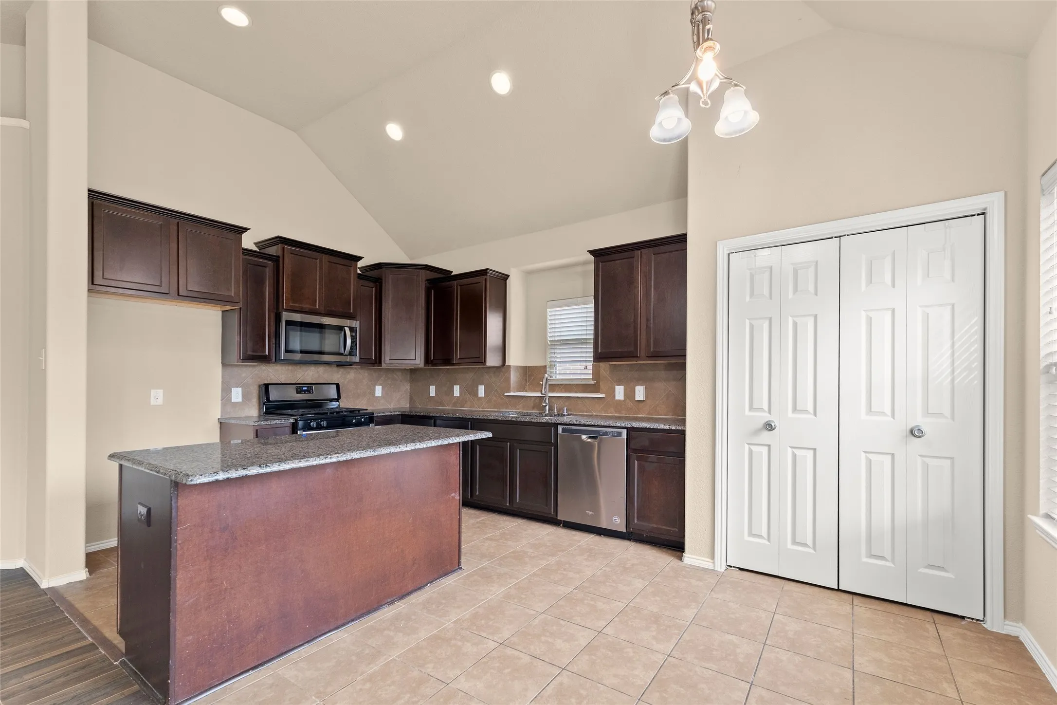 Kitchen with vaulted ceiling, dark brown cabinets, dark stone counters, stainless steel appliances, and backsplash