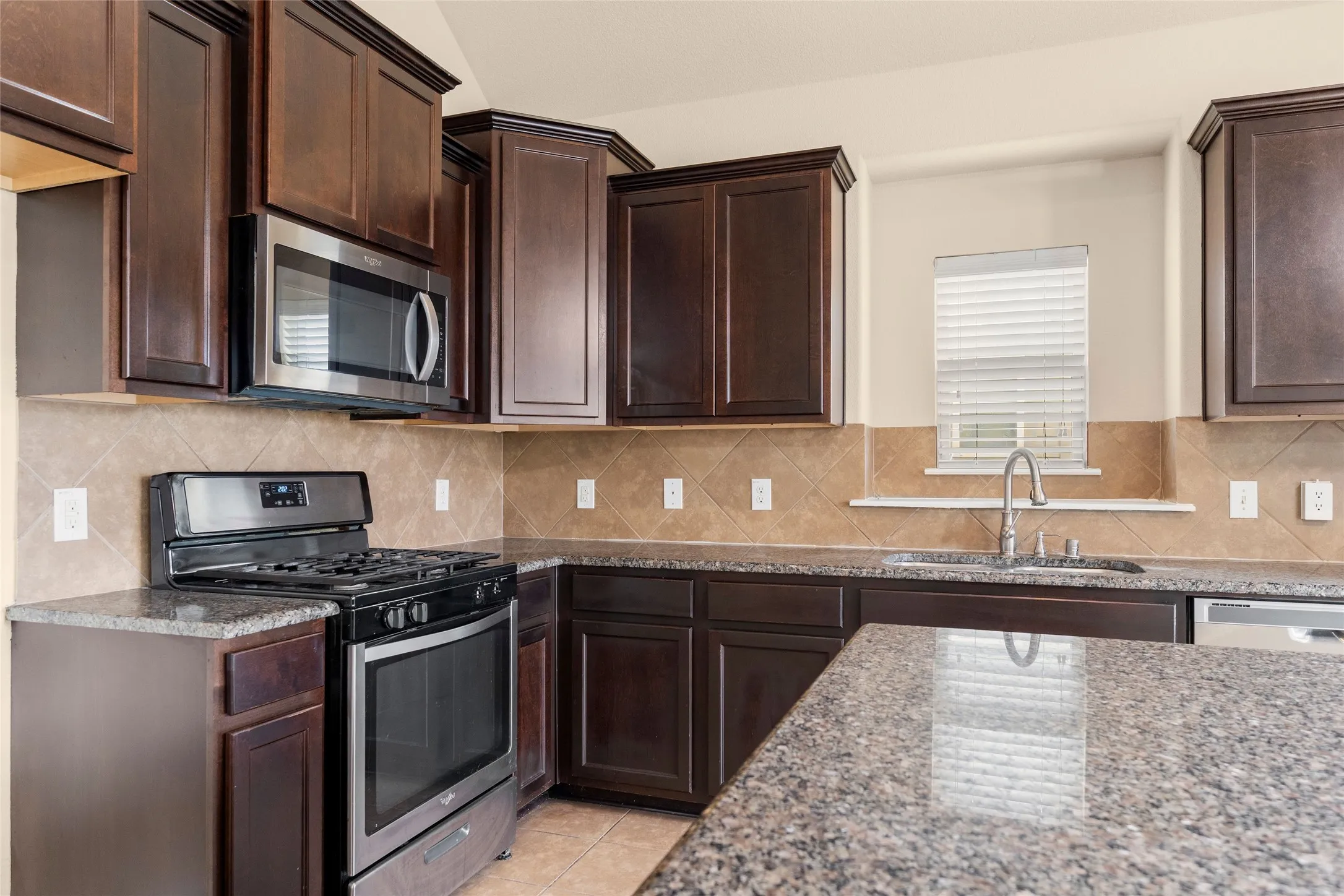 Kitchen with appliances with stainless steel finishes, dark brown cabinets, decorative backsplash, and dark stone countertops