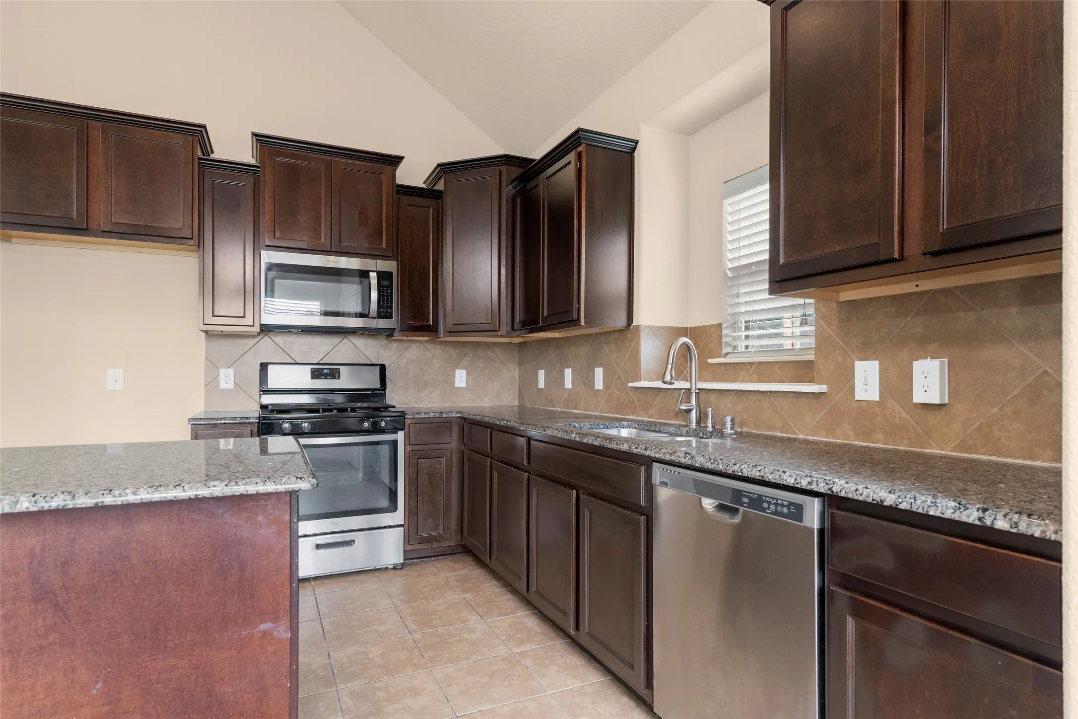 Kitchen featuring appliances with stainless steel finishes, decorative backsplash, dark brown cabinetry, dark stone countertops, and light tile patterned flooring