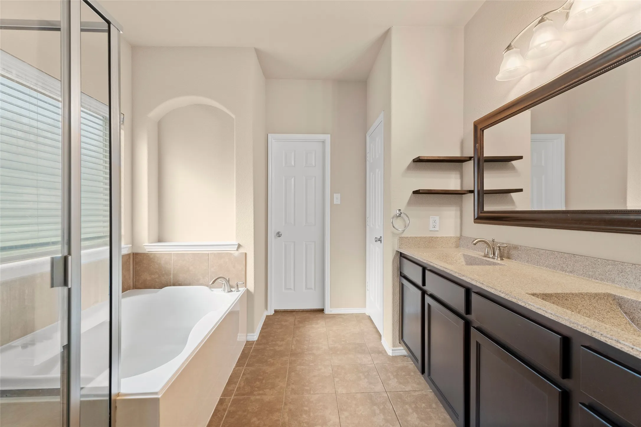 Full bath featuring a bath, double vanity, light tile patterned floors, and a stall shower