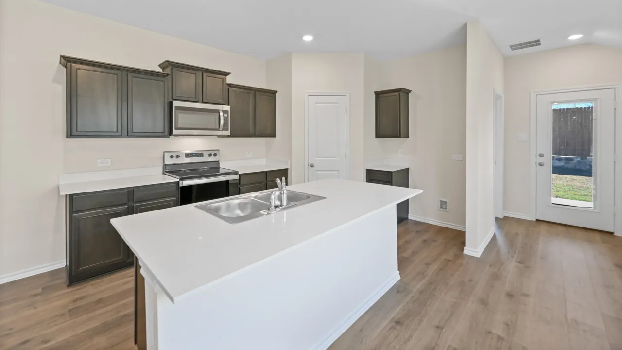 Kitchen featuring a central island with a double basin sink, dark wood cabinetry, stainless steel appliances, light countertops, and wood-finish flooring