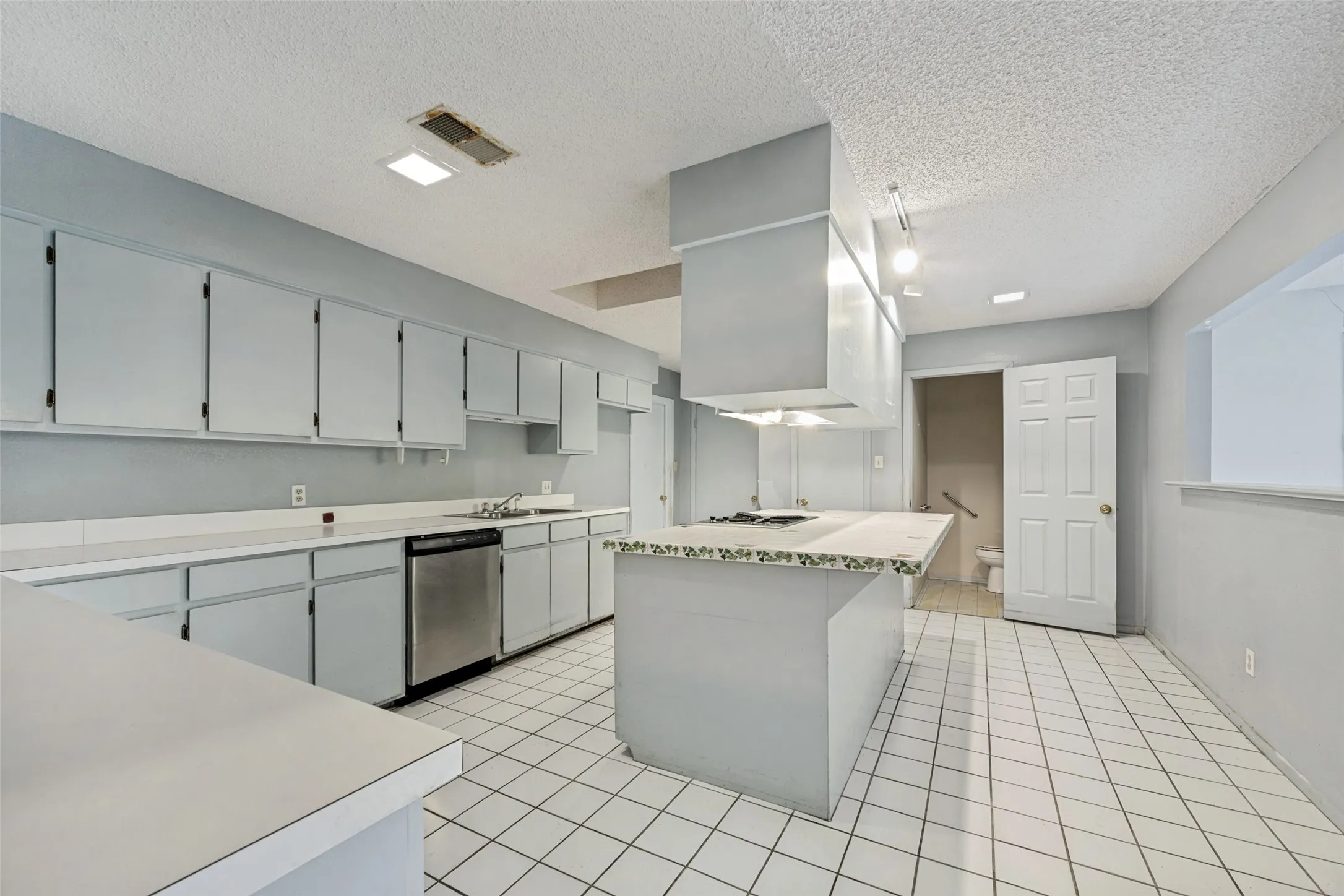 Kitchen featuring extensive cabinetry, white countertops, a center island with cooktop, stainless steel dishwasher, and tiled flooring