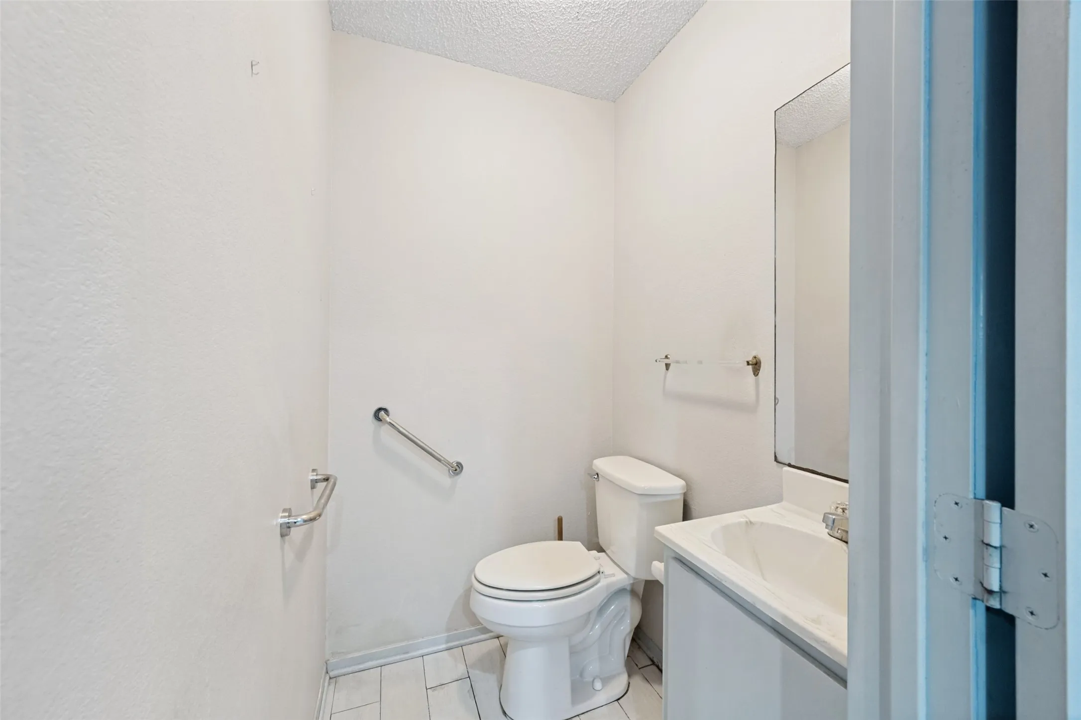 Bathroom featuring a vanity with an integrated sink, wall-mounted mirror, white toilet, and tile flooring