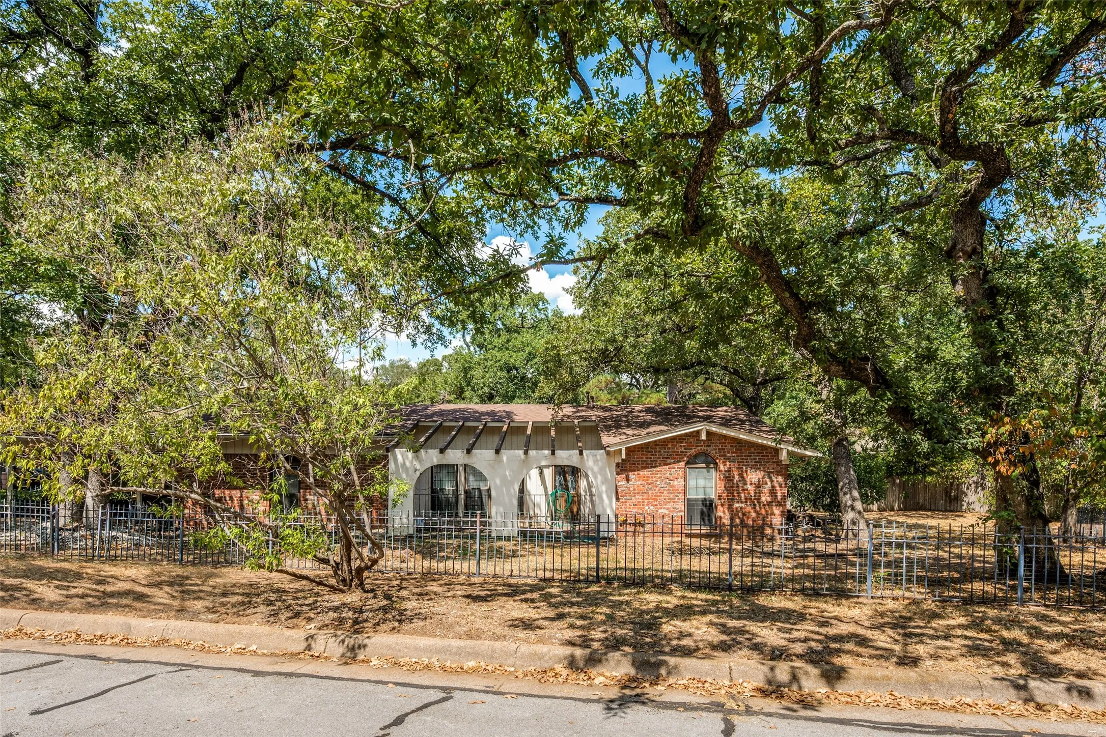 Brick exterior with arched window, decorative pergola, and mature trees