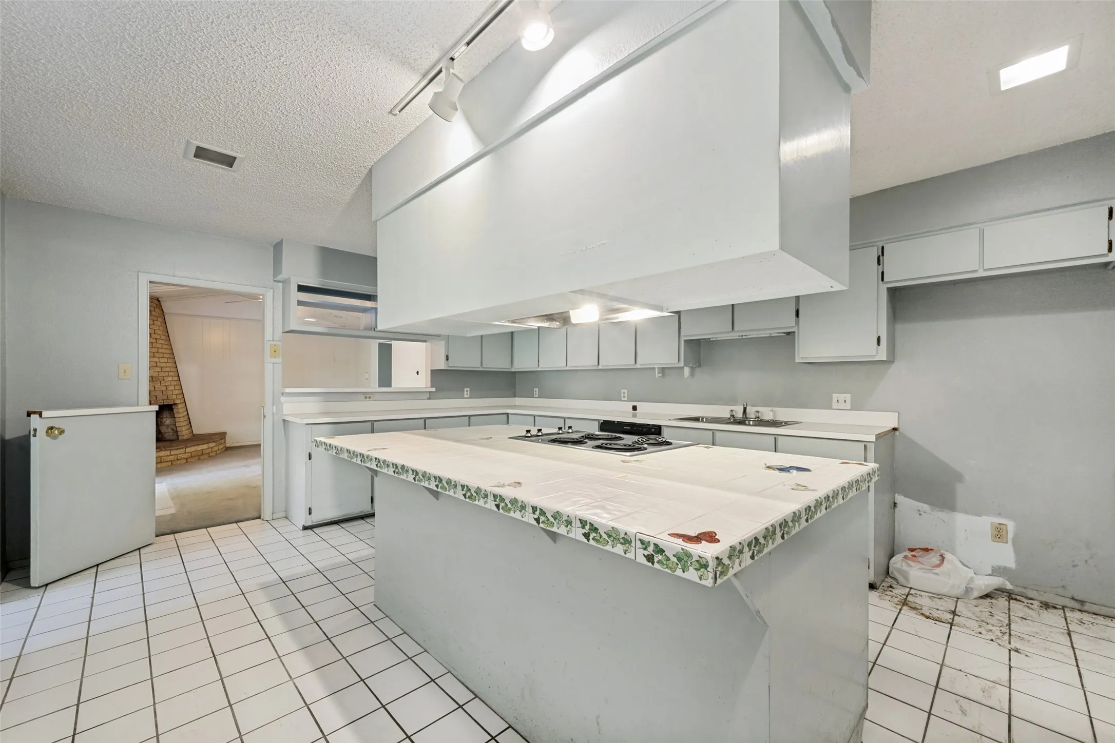Kitchen featuring white tile flooring, built-in cabinetry, an island with cooktop, and track lighting