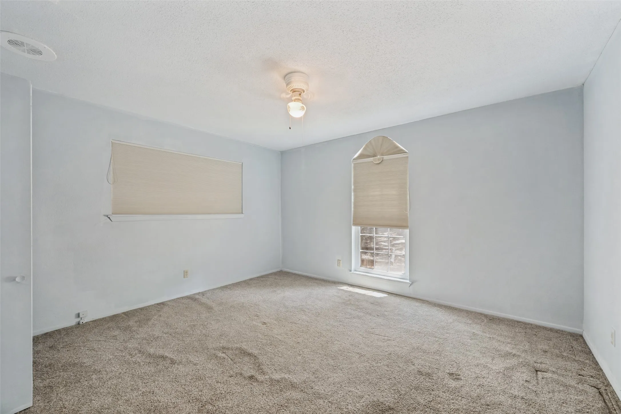 Spacious room with carpeted flooring, two windows with blinds, and ceiling fan light fixture