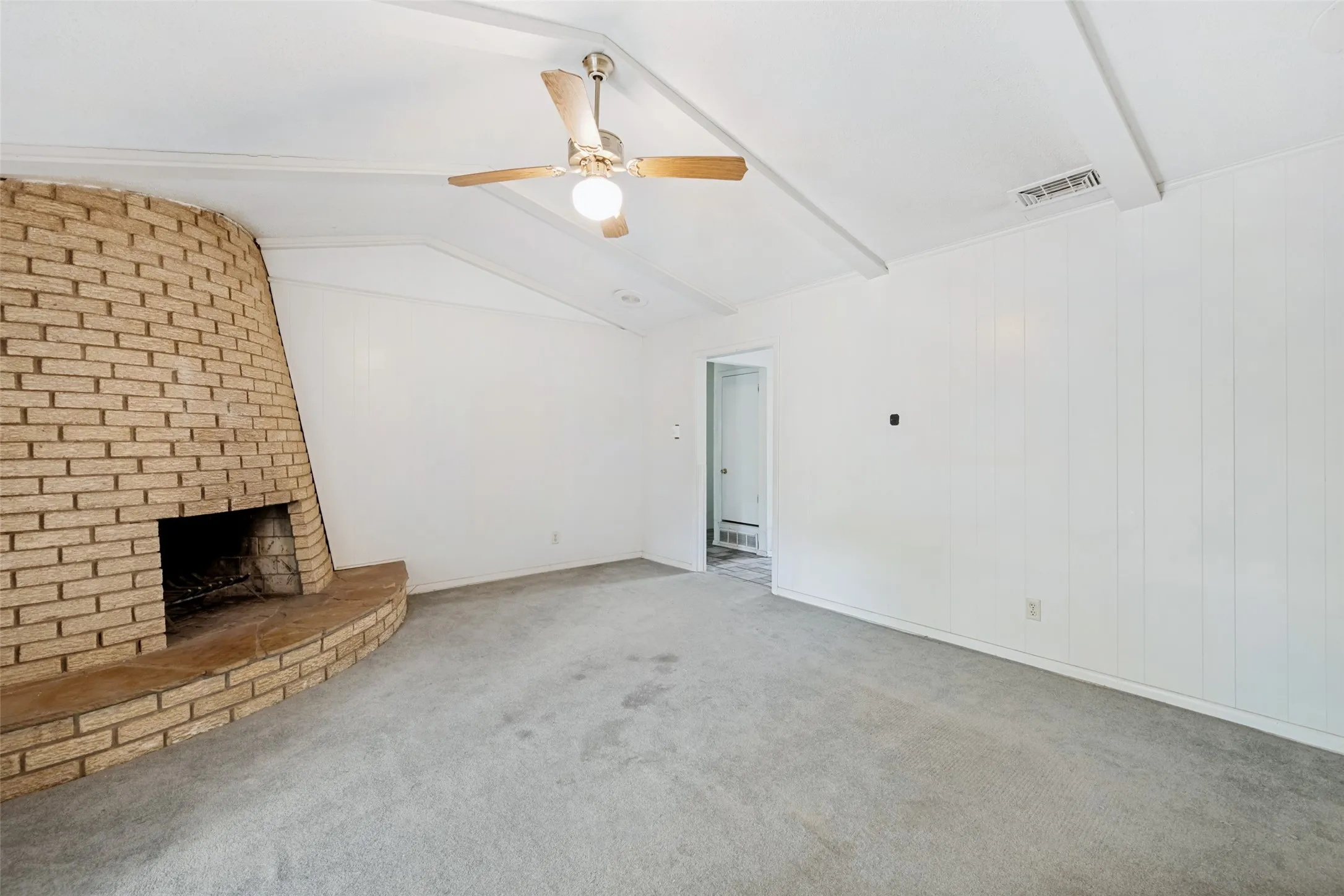 Brick fireplace with hearth, vaulted ceiling with exposed beams, ceiling fan with light fixture, and vertical paneling
