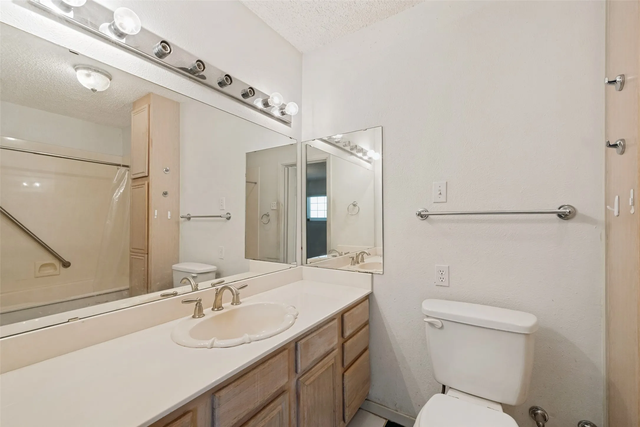 Vanity with integrated sink, extensive mirror, full-width vanity lighting, built-in storage cabinetry, and a shower with grab bar