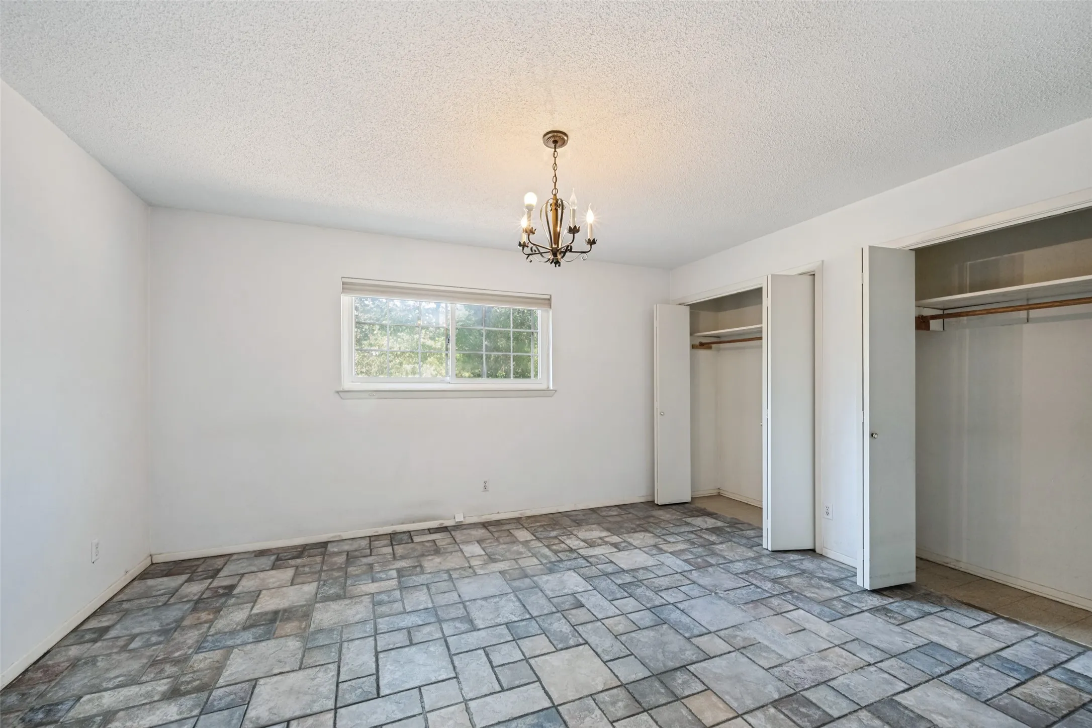 Patterned tile flooring, single window, chandelier lighting, and two built-in closets with bi-fold doors