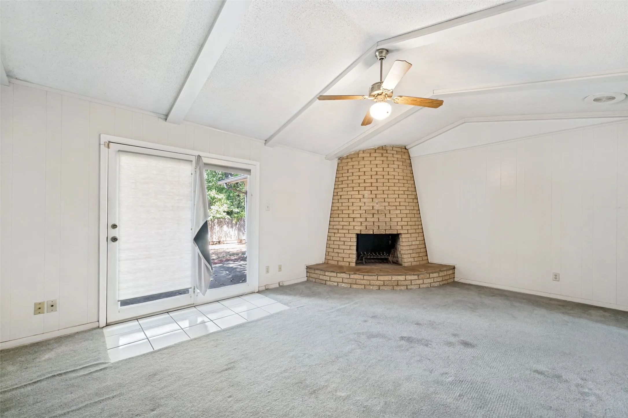 Vaulted ceiling with exposed beams, brick fireplace, ceiling fan, sliding glass door, and tiled entry