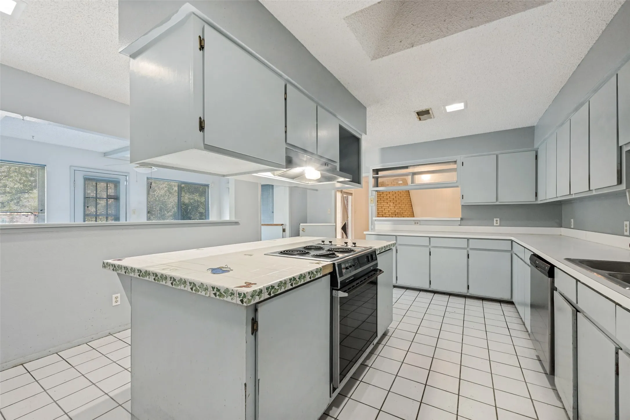 Kitchen featuring an island with a built-in electric range, extensive cabinetry, tile flooring, and a skylight