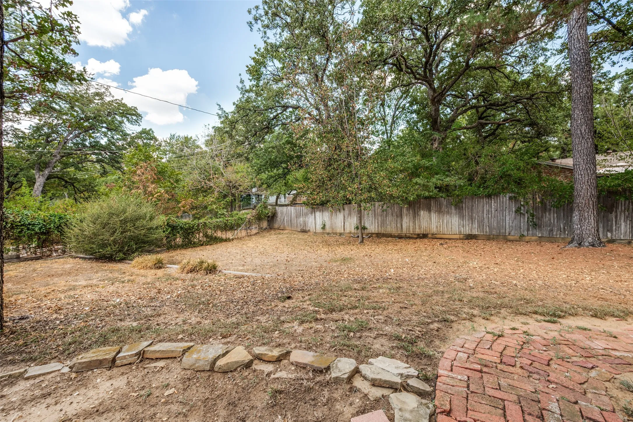 Private backyard with mature trees, wood fence, and a brick patio