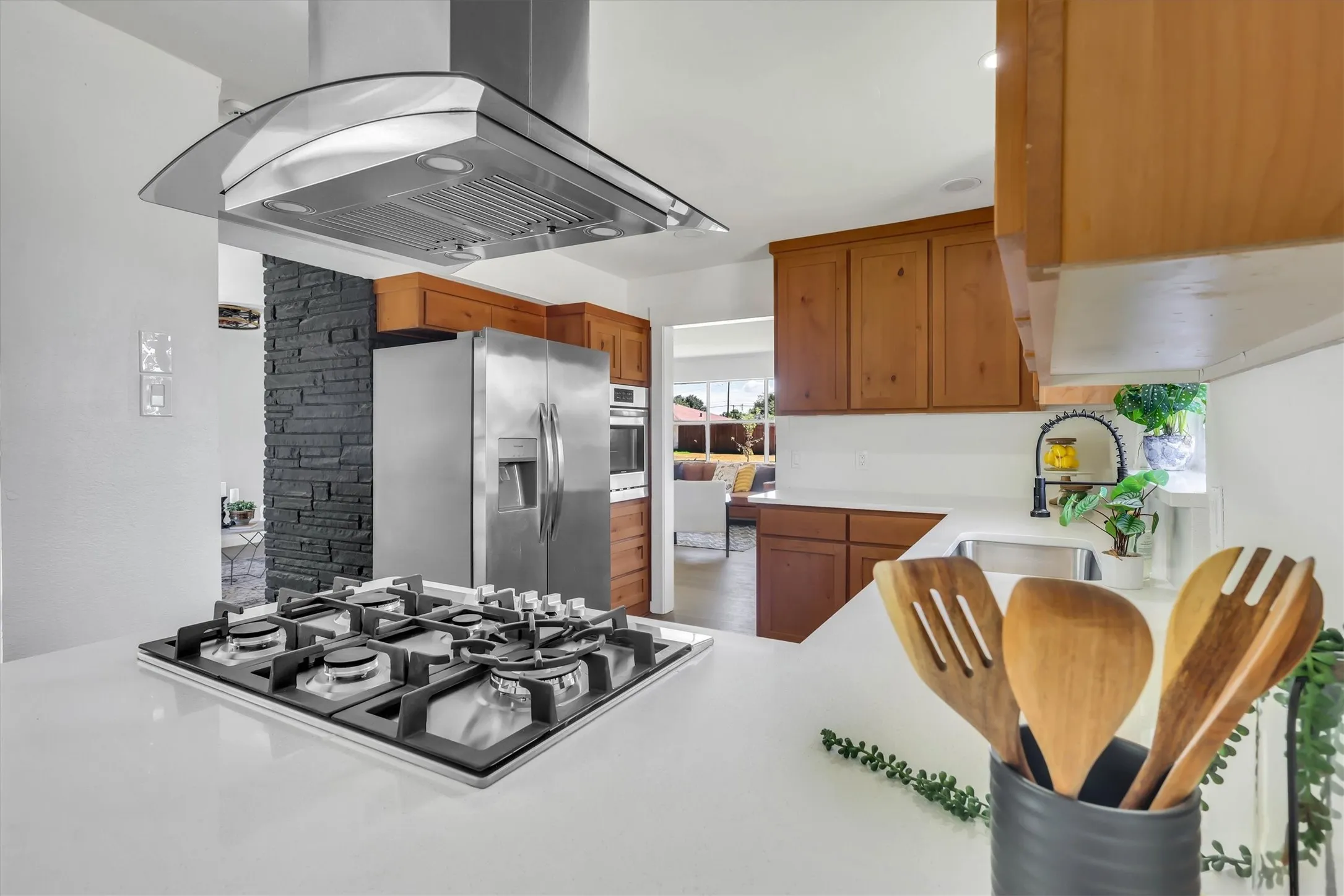 Stainless steel appliances, built-in cooktop, light wood-finish cabinetry, under-cabinet sink, and stone accent wall