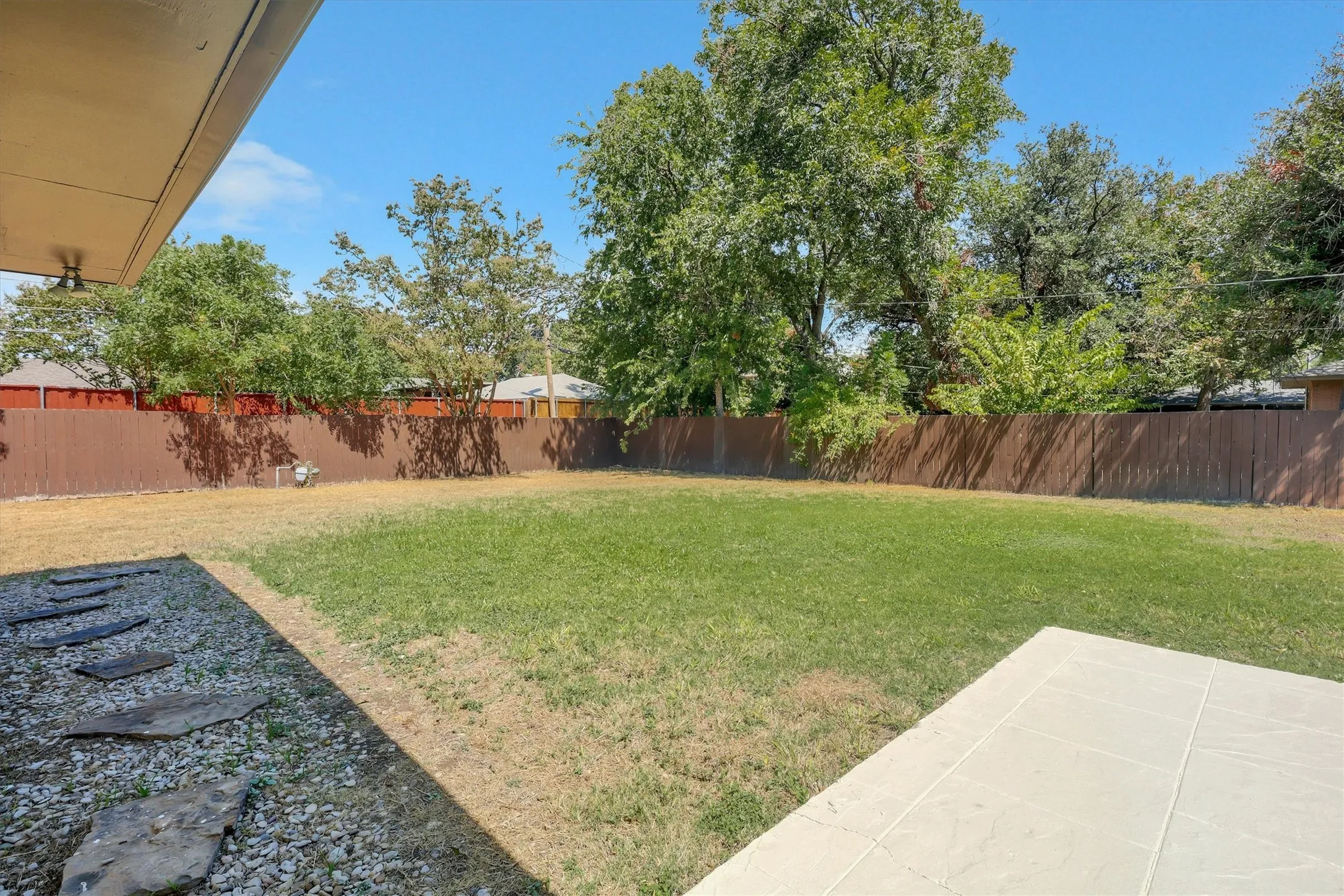 Expansive backyard featuring a privacy fence, established trees, a concrete patio, and natural stone pavers
