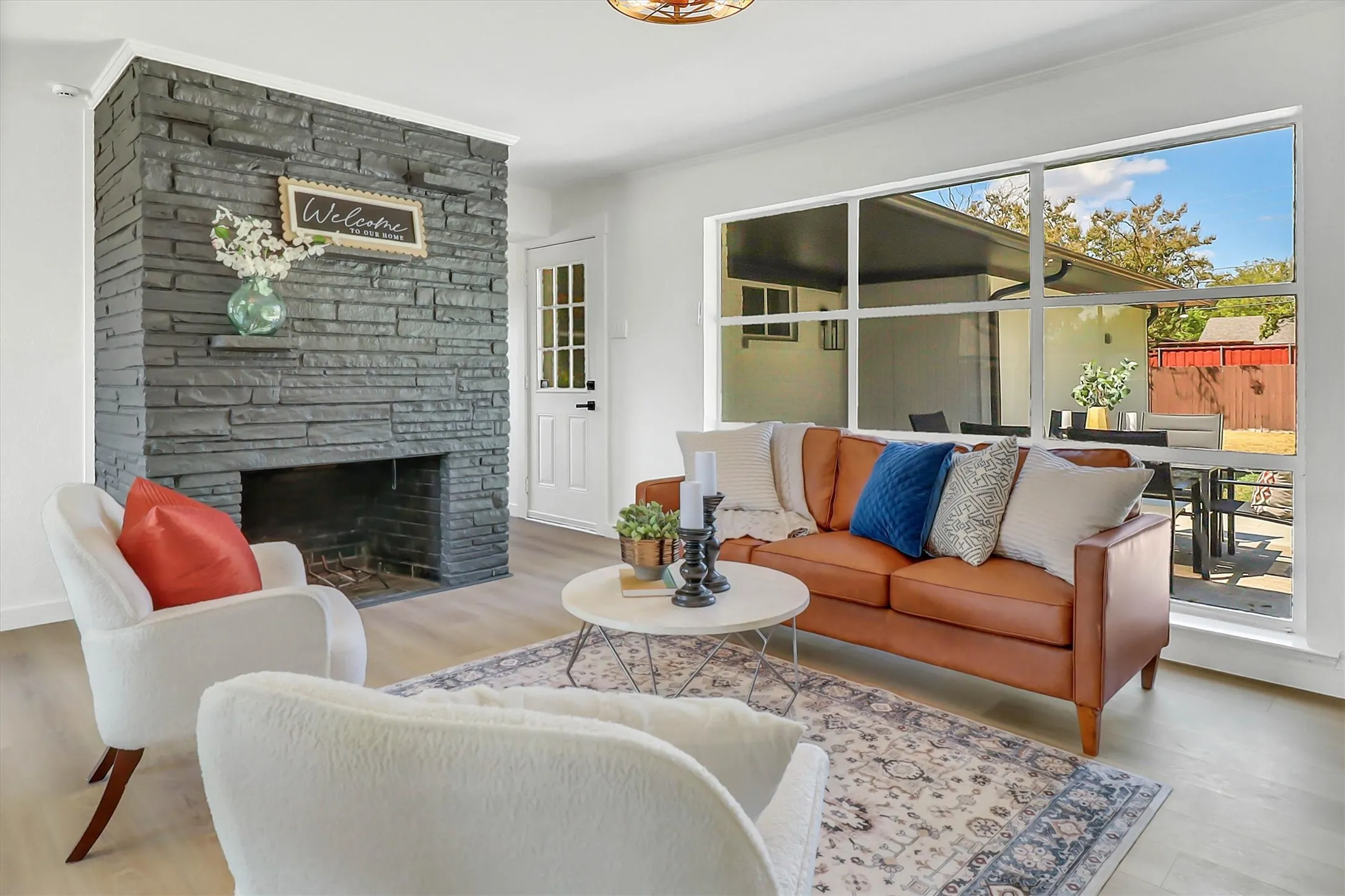 Stacked stone fireplace with a hearth, light-toned wood-finish flooring, and a multi-pane picture window