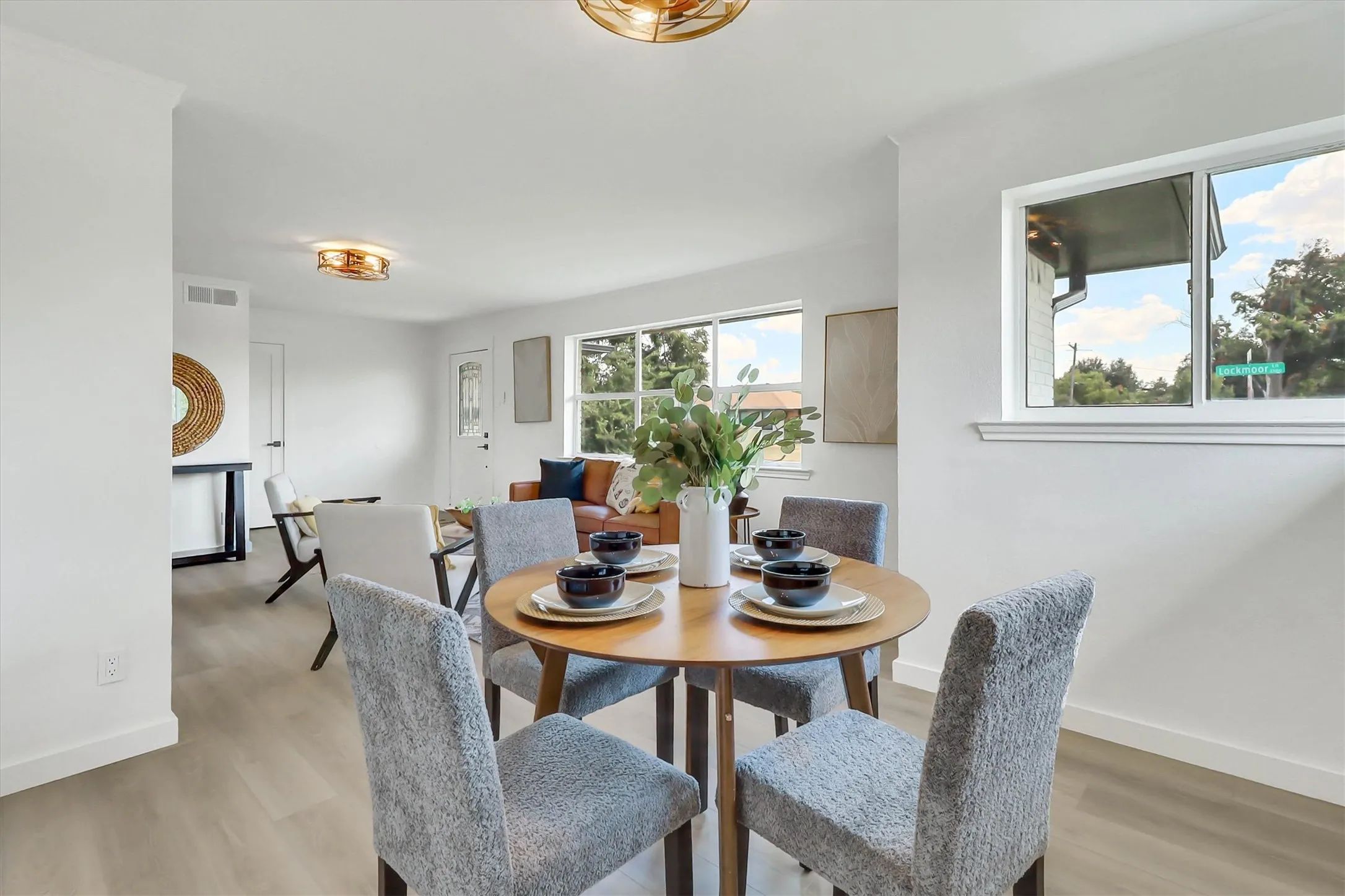 Open-concept living space with light wood-finish flooring, white walls, and contemporary light fixtures